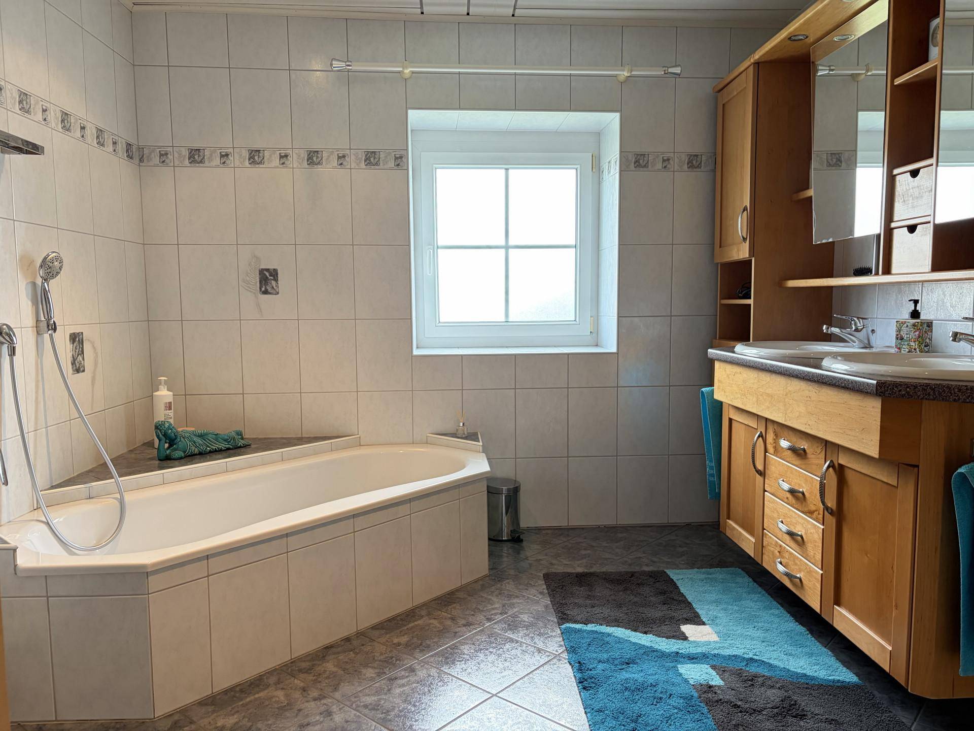 Geräumiges Badezimmer mit Eckbadewanne, Doppelwaschbecken und Fenster für Tageslicht.