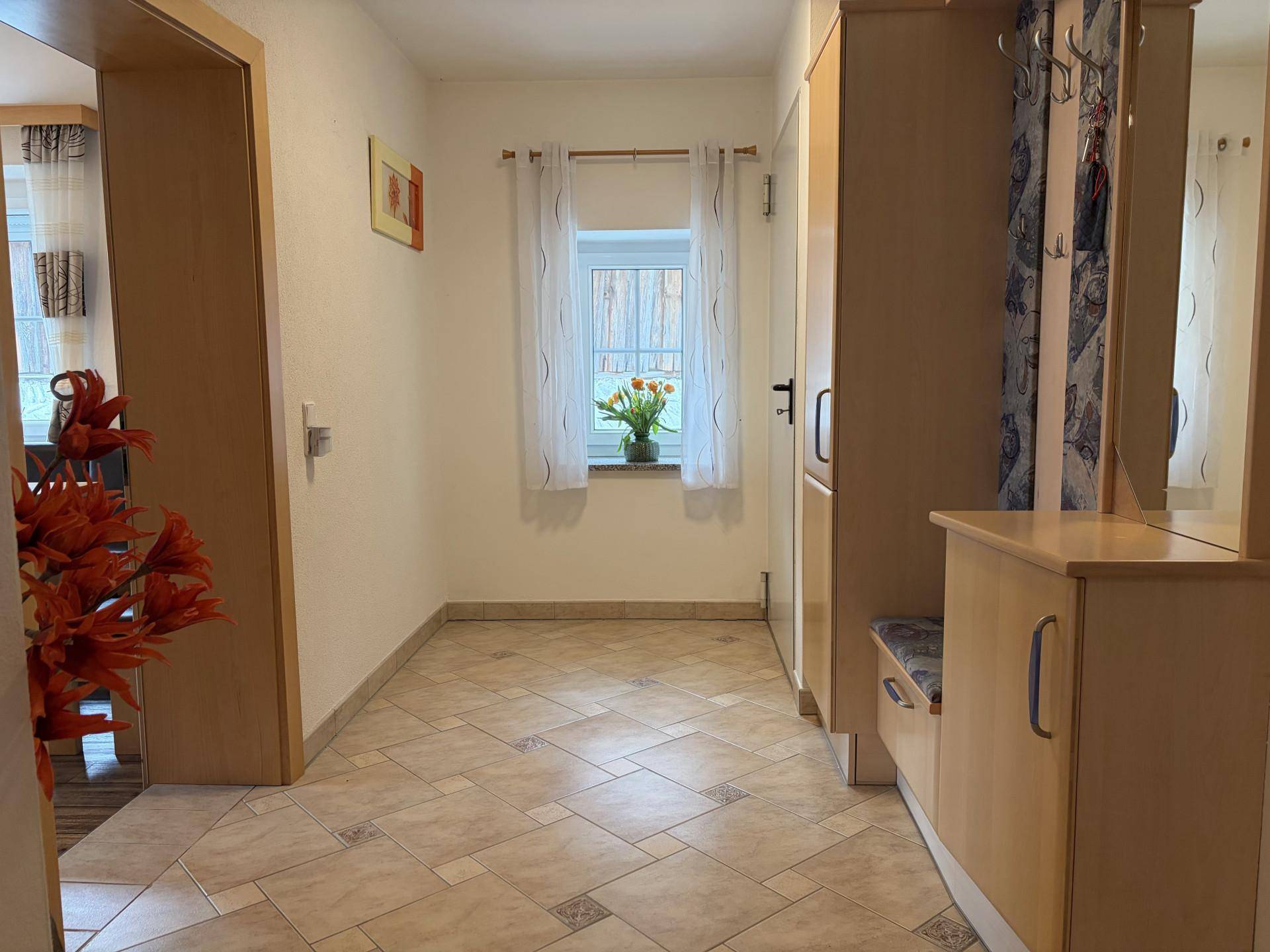 Heller Flur mit Fliesenboden, Garderobe und Fenster mit Blick ins Grüne.