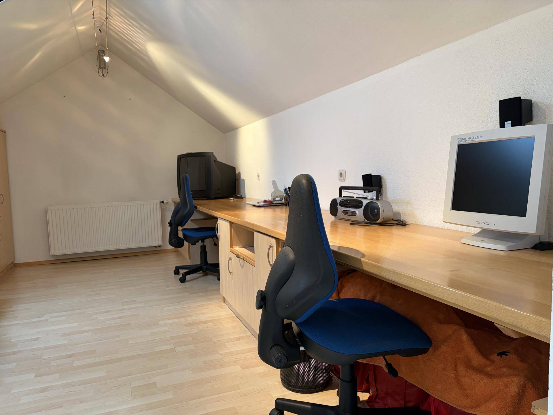 Dachgeschoss-Büro mit schrägen Wänden, Holzschreibtisch und Blick auf die Umgebung.