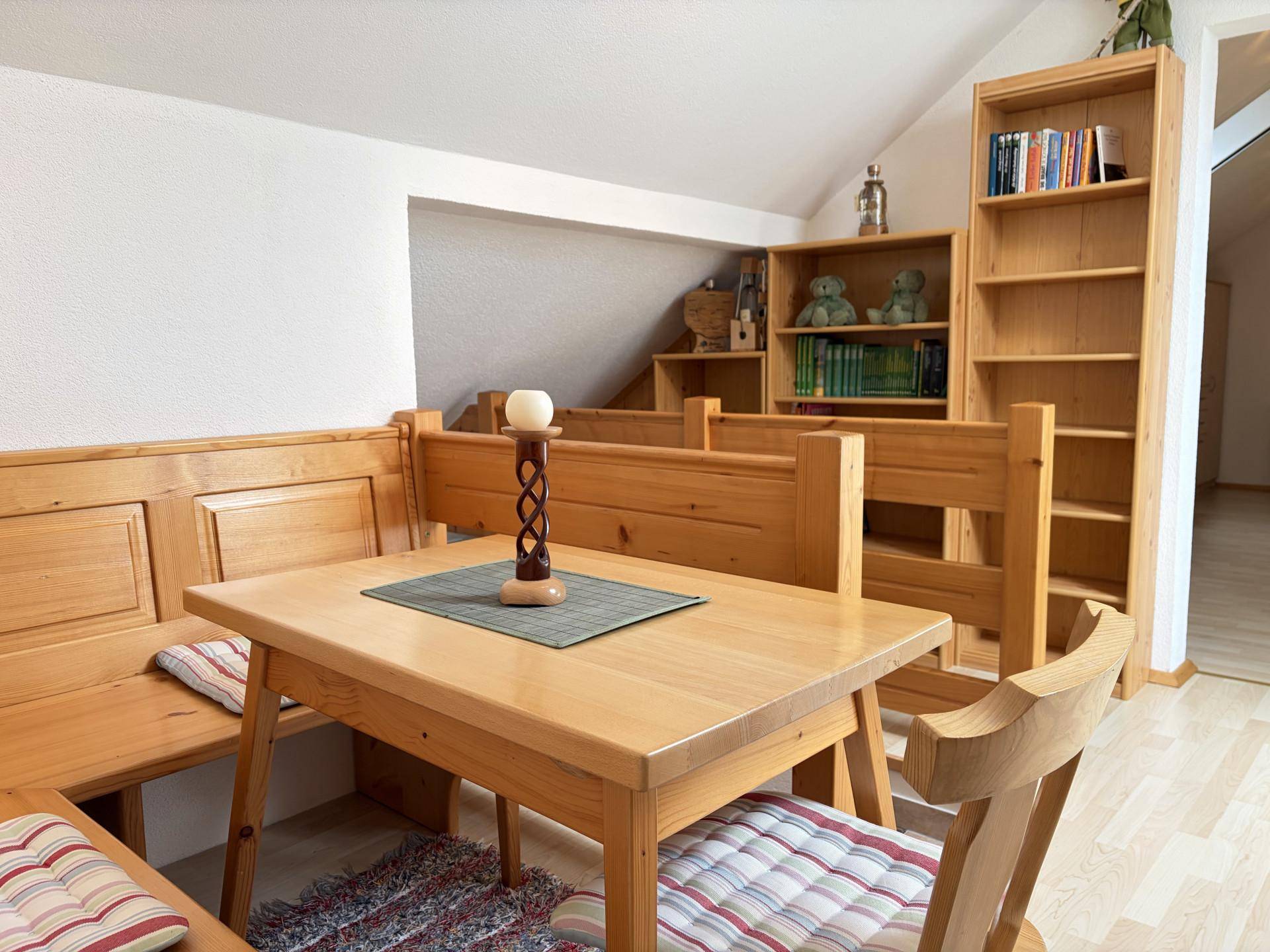 Gemütlicher Essbereich im Dachgeschoss mit Holztisch, Eckbank und Bücherregalen.