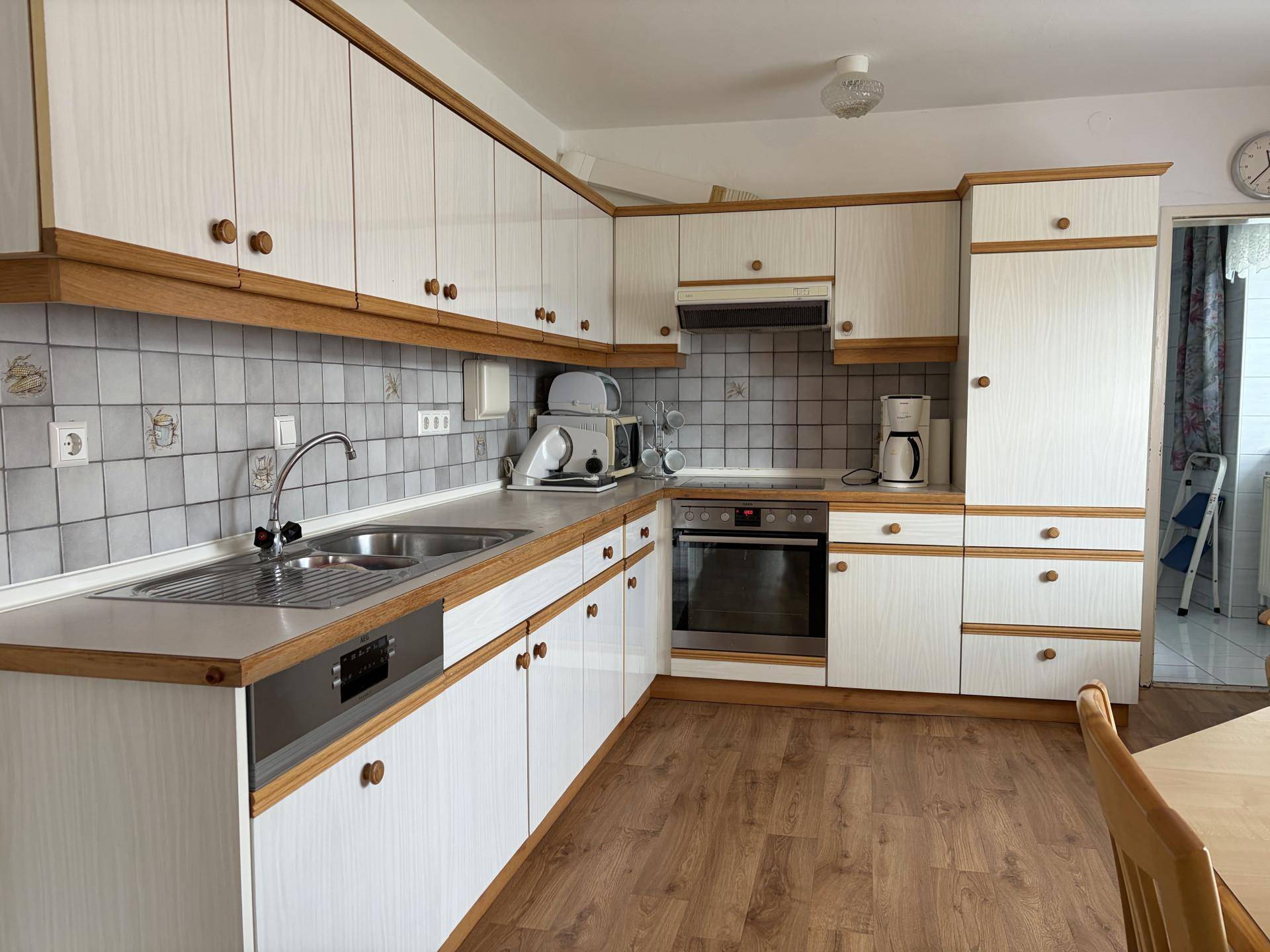 Funktionale Küche mit weißen Schränken, Holzakzenten und Fliesenrückwand.