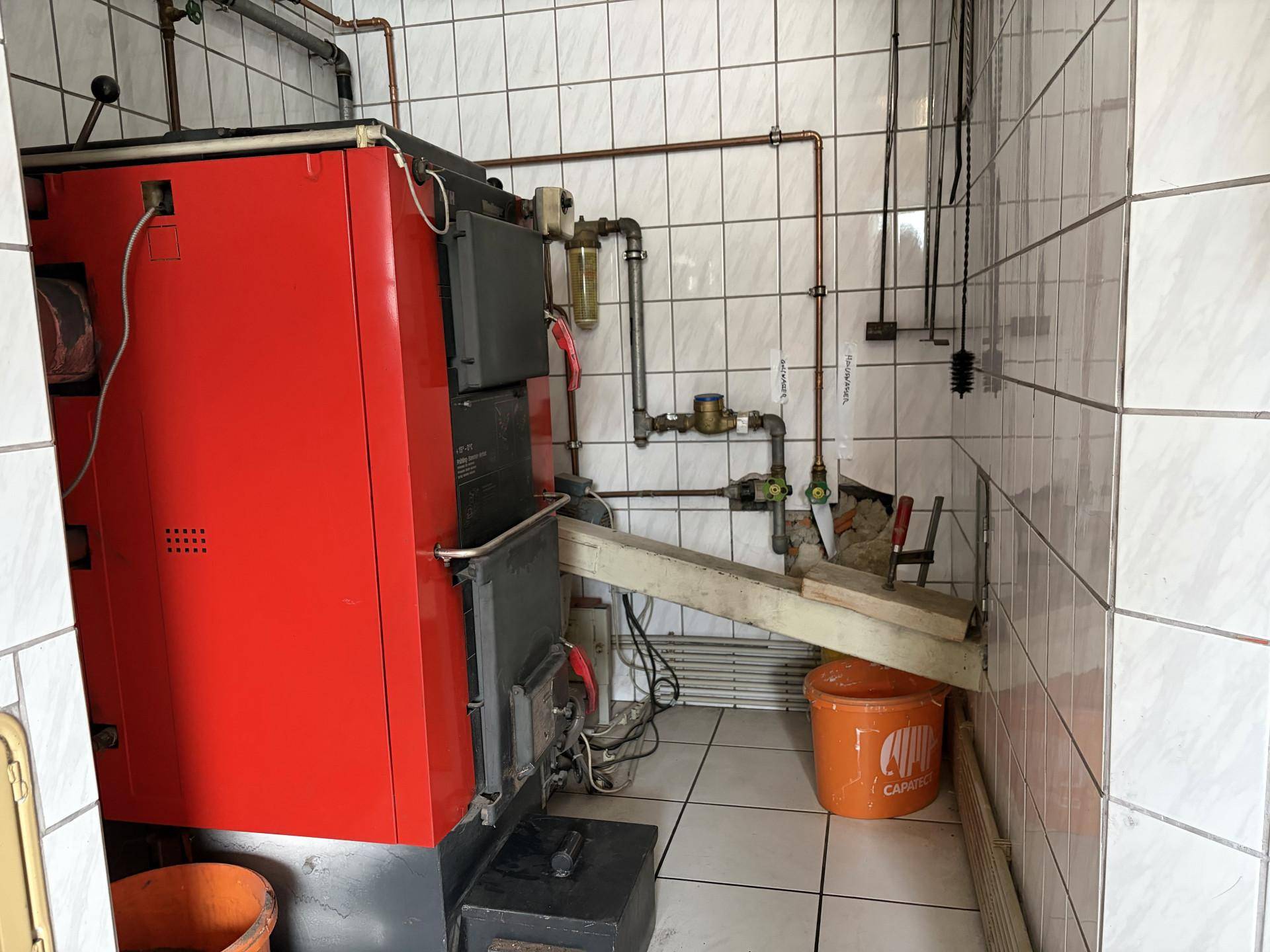 Heizungsraum im Keller mit großem Heizkessel und Fliesenwänden.