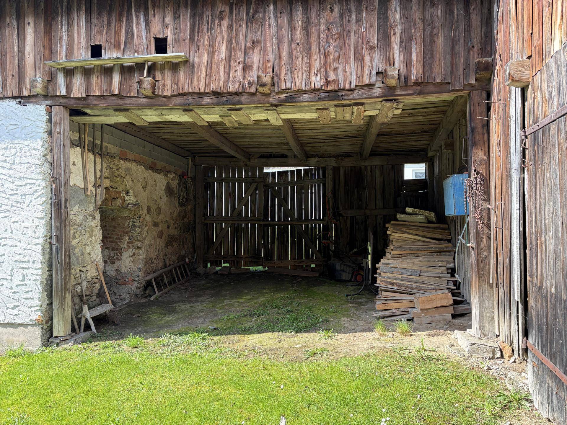 Offener Scheunenbereich mit Holzbalken und Lagerfläche für Holz.