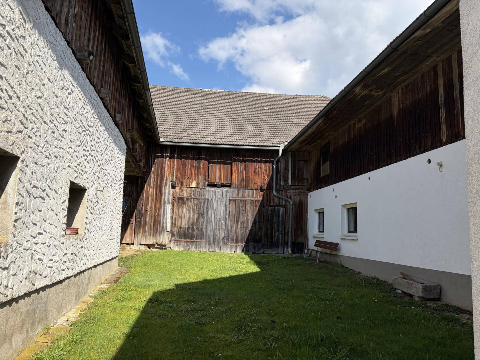 Grüner Innenhof zwischen zwei Gebäuden mit Holzwänden und Rasenfläche.