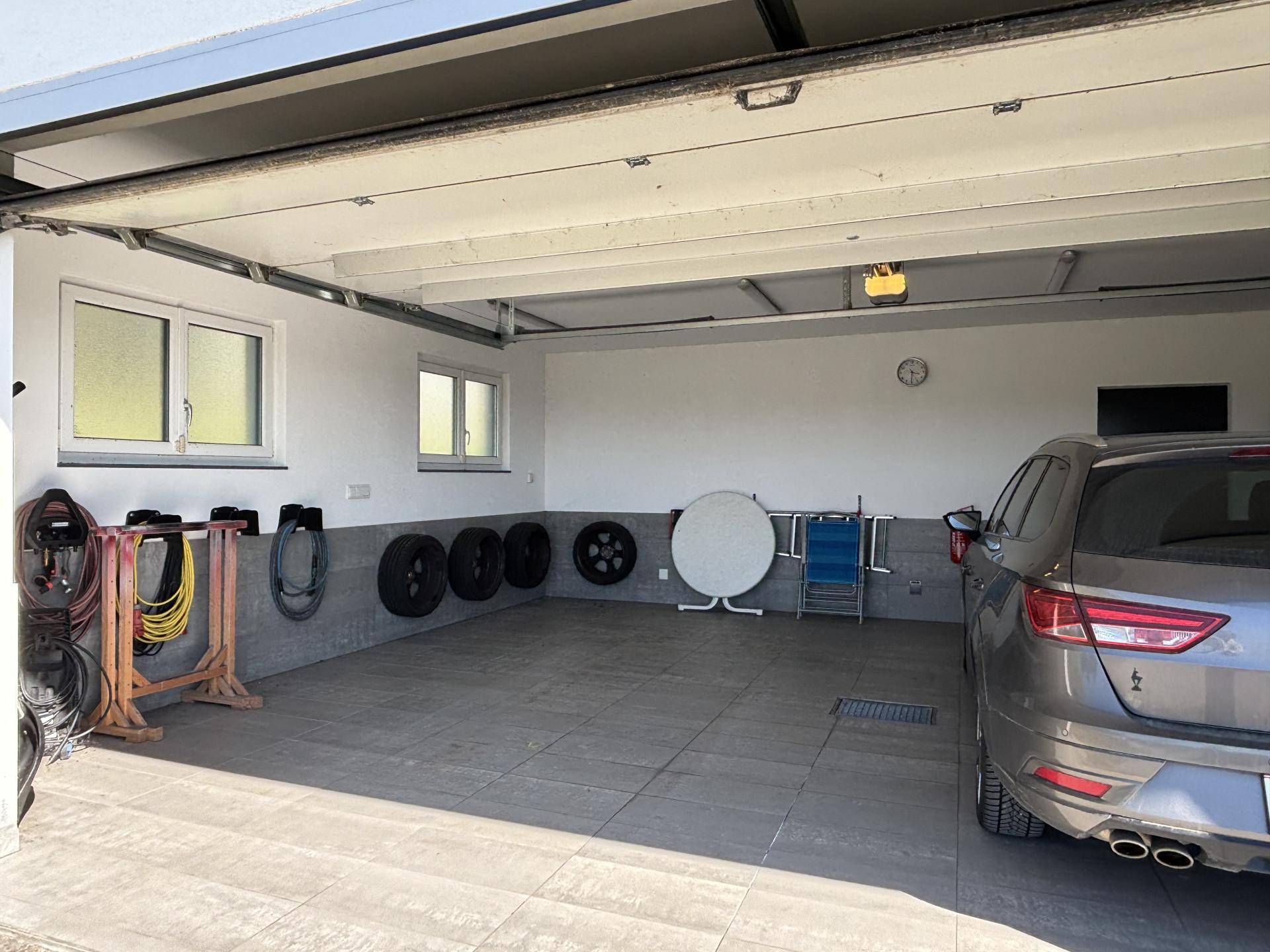 Geräumige Garage mit Platz für ein Fahrzeug, Fliesenboden und praktischen Lagerbereichen.