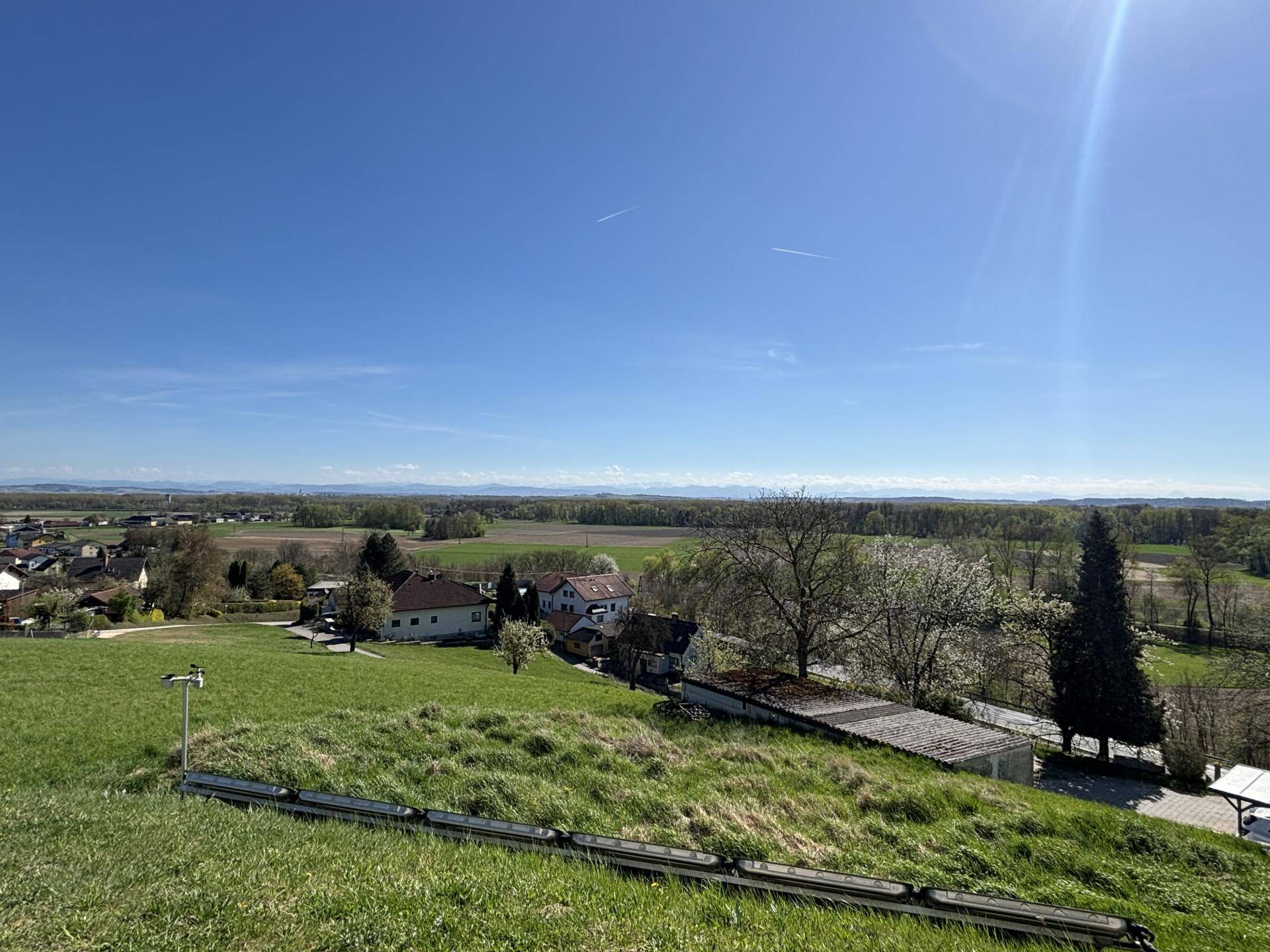 Grüne Wiese mit Blick auf die weite Landschaft und entfernte Berge unter strahlend blauem Himmel.