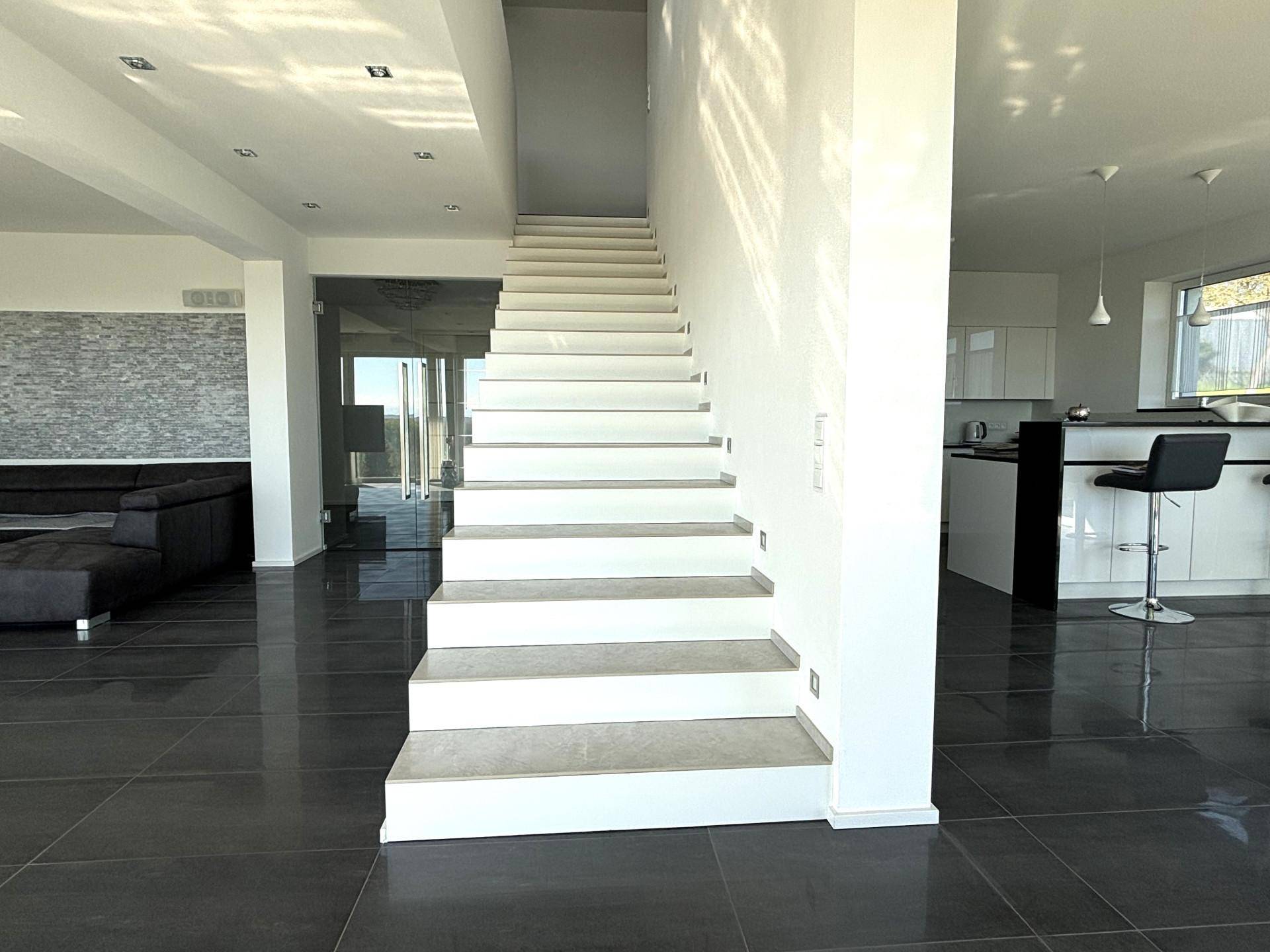 Elegante, schwebende Treppe in einem offenen Wohnbereich, verbindet die Etagen und führt zur Küche.