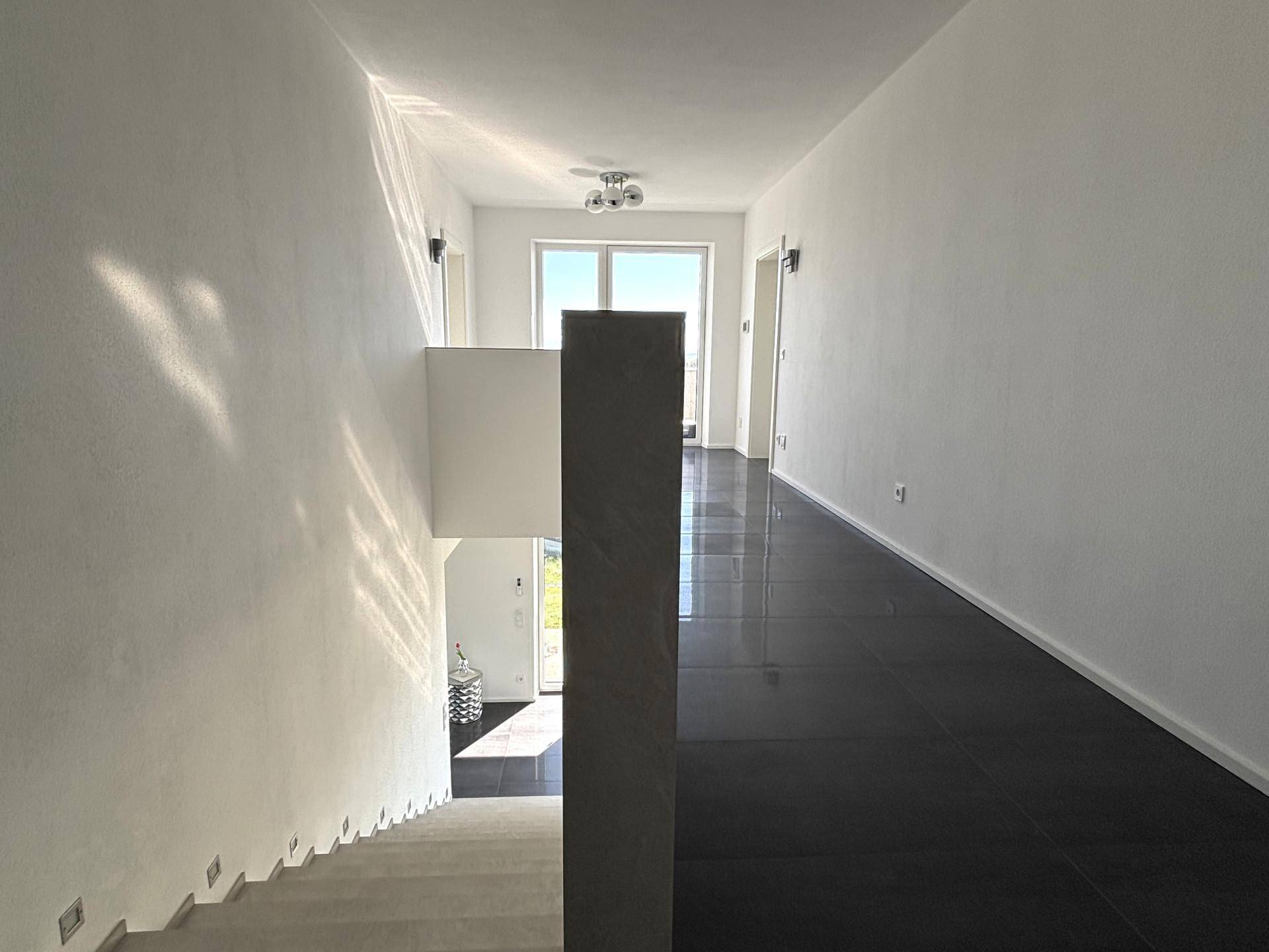 Heller Flur im Obergeschoss mit dunklen Fliesen und Blick auf die Treppe, die nach unten führt.