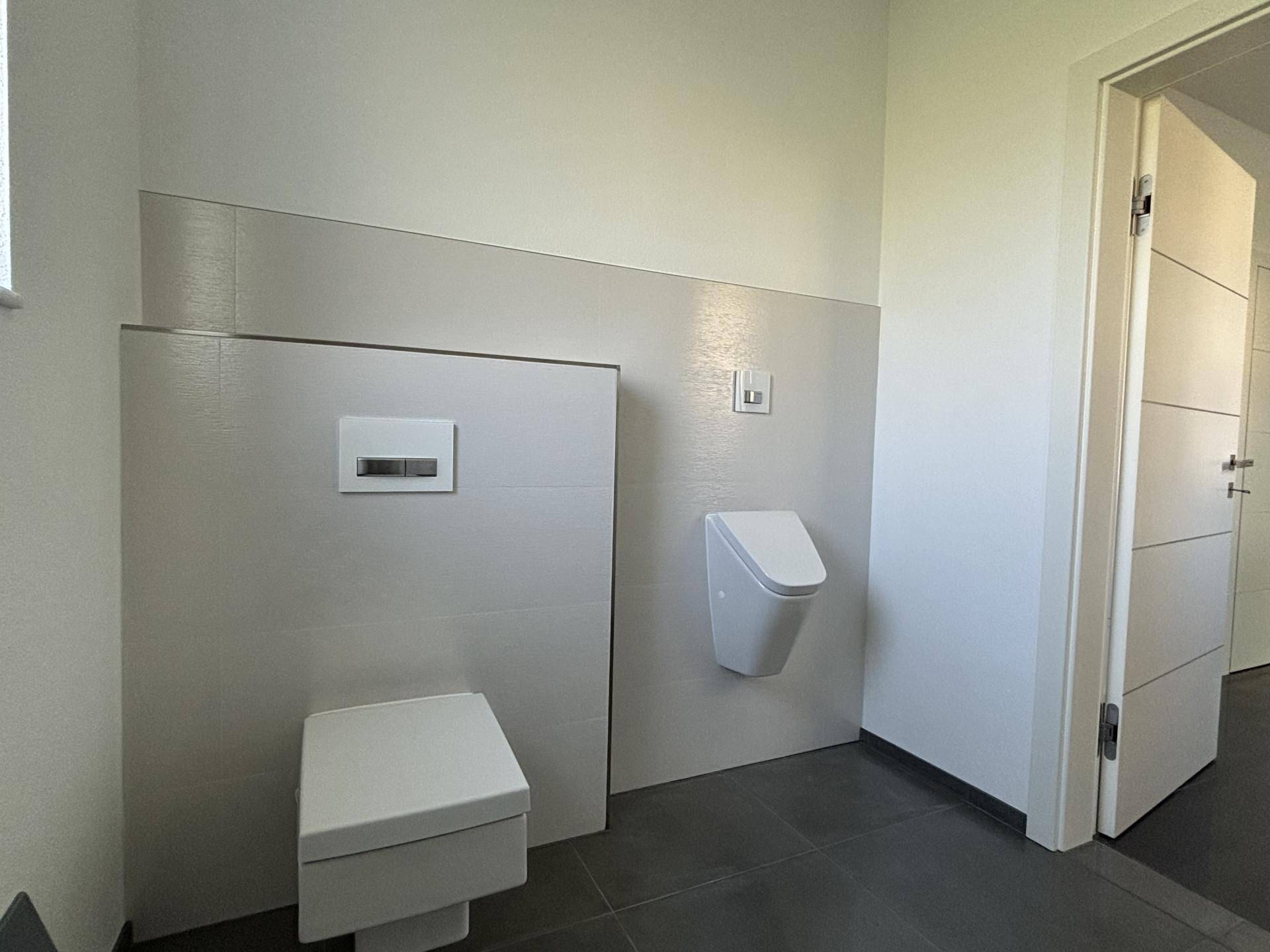 Modernes Gäste-WC mit wandhängendem WC und Urinal, in minimalistischem Design gehalten.