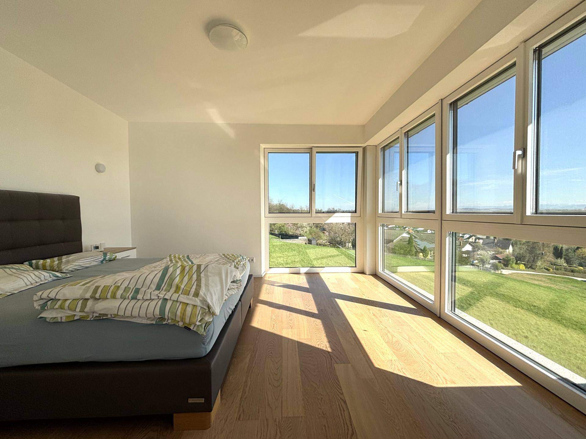 Helles Schlafzimmer mit großen Fenstern und Holzboden, bietet einen weiten Blick ins Grüne.