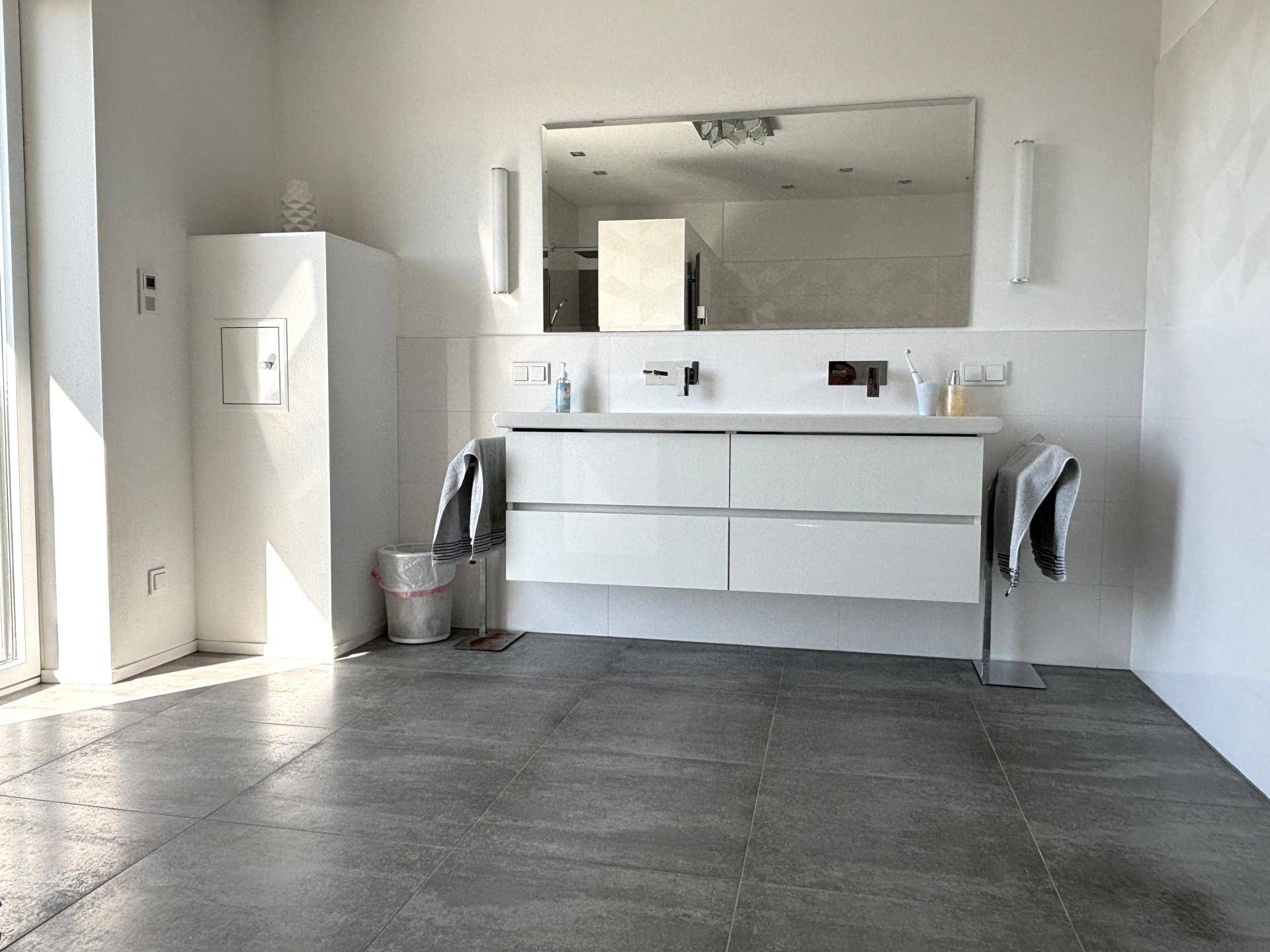 Helles Badezimmer mit modernem Doppelwaschtisch, großem Spiegel und grauen Bodenfliesen.