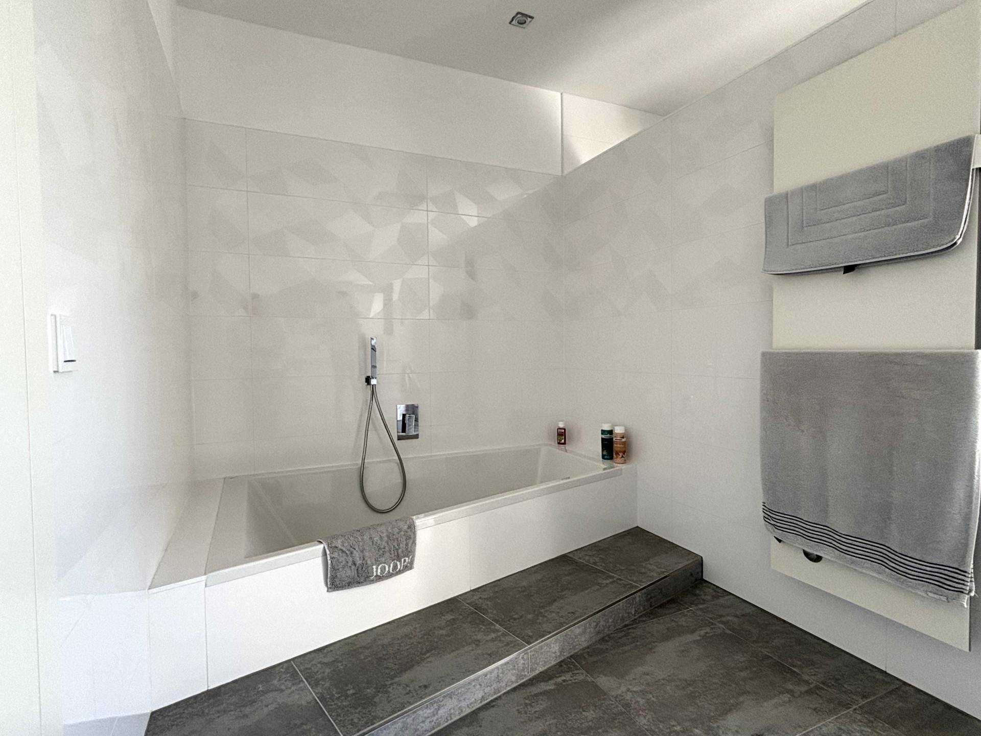 Modernes Badezimmer mit integrierter Badewanne, weißen Wandfliesen und beheiztem Handtuchhalter.