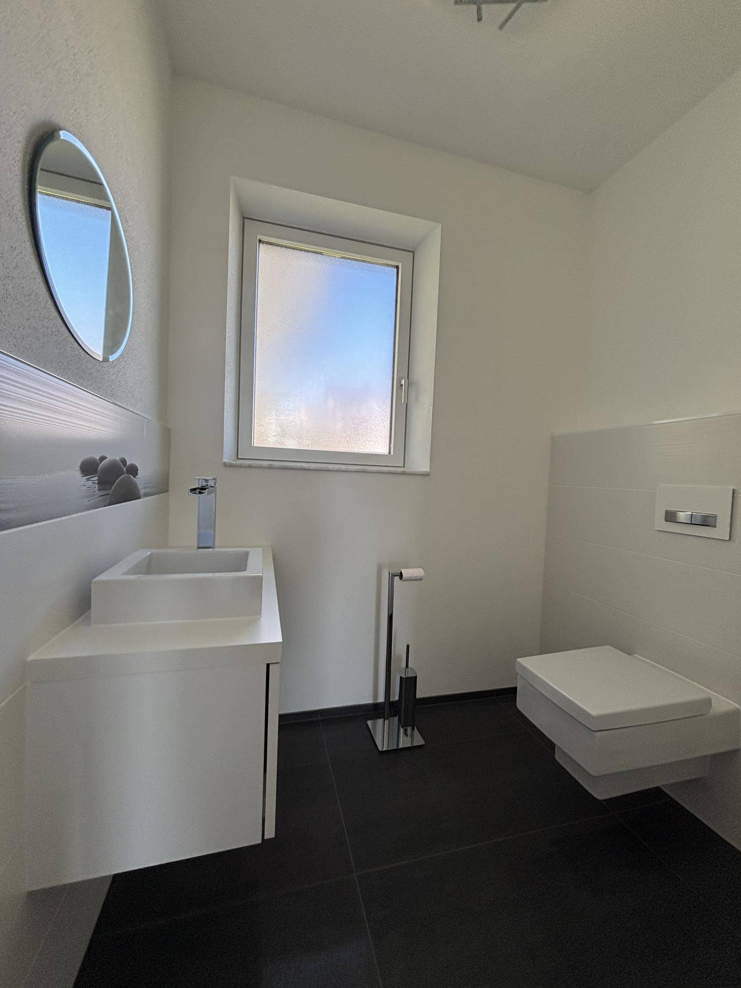 Modernes Gäste-WC mit wandhängender Toilette, kleinem Waschbecken und Fenster für Tageslicht.