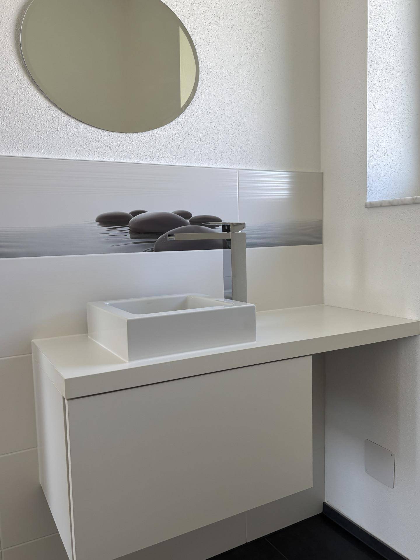 Detailansicht des modernen Waschbeckens im Gäste-WC mit minimalistischem Design und rundem Spiegel.