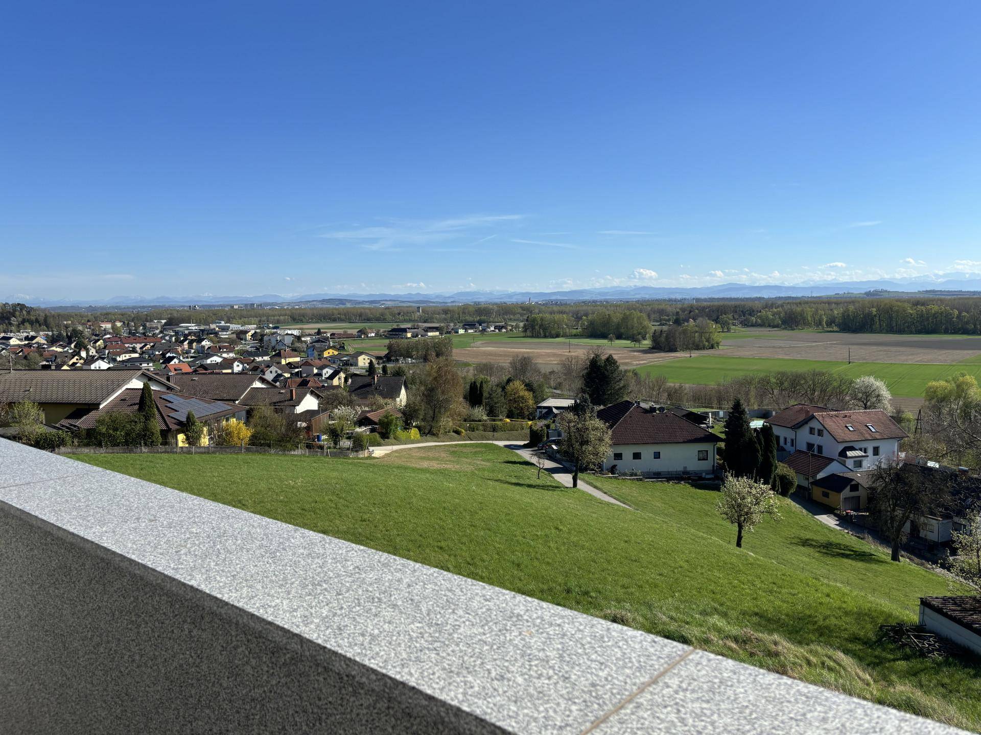 Panoramablick von der Terrasse über ein Dorf, weite Felder und die umliegende Berglandschaft.