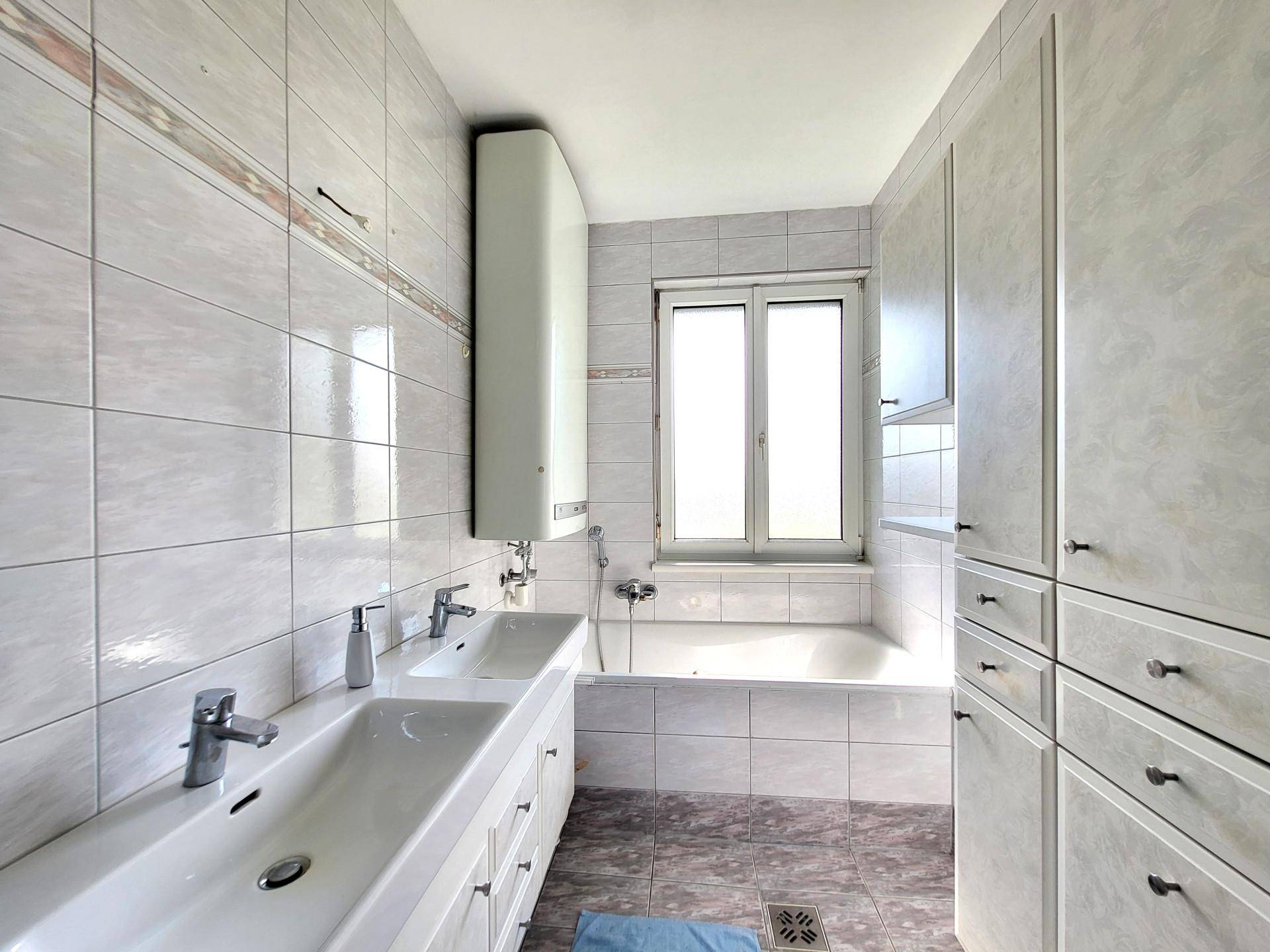 Gefliestes Badezimmer mit Doppelwaschbecken, Badewanne und großem Spiegelschrank.