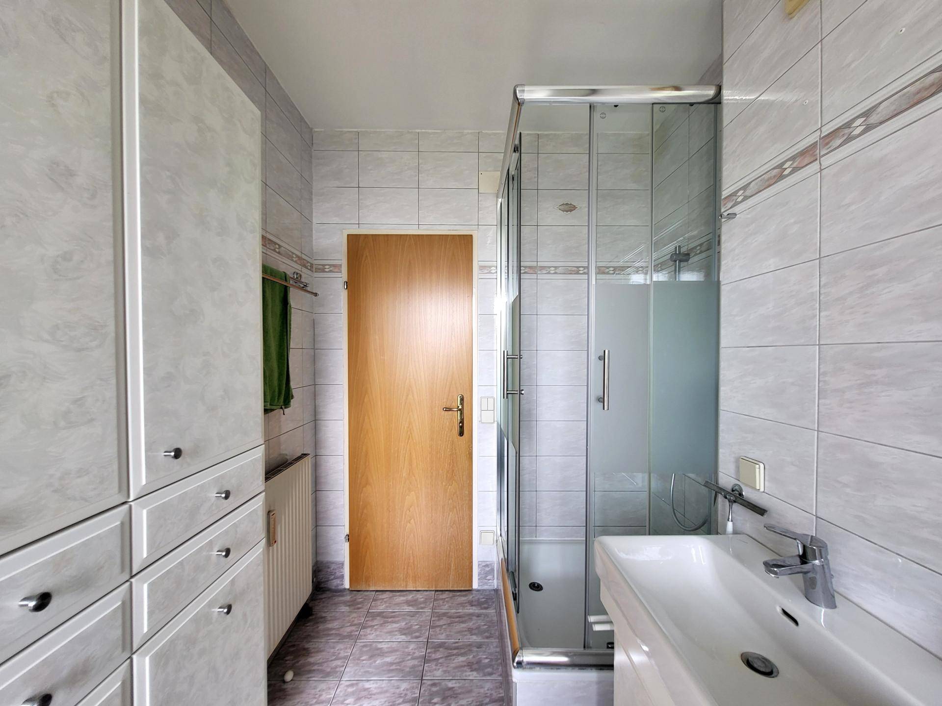 Funktionales Badezimmer mit Duschkabine, Waschbecken und praktischen Einbauschränken.
