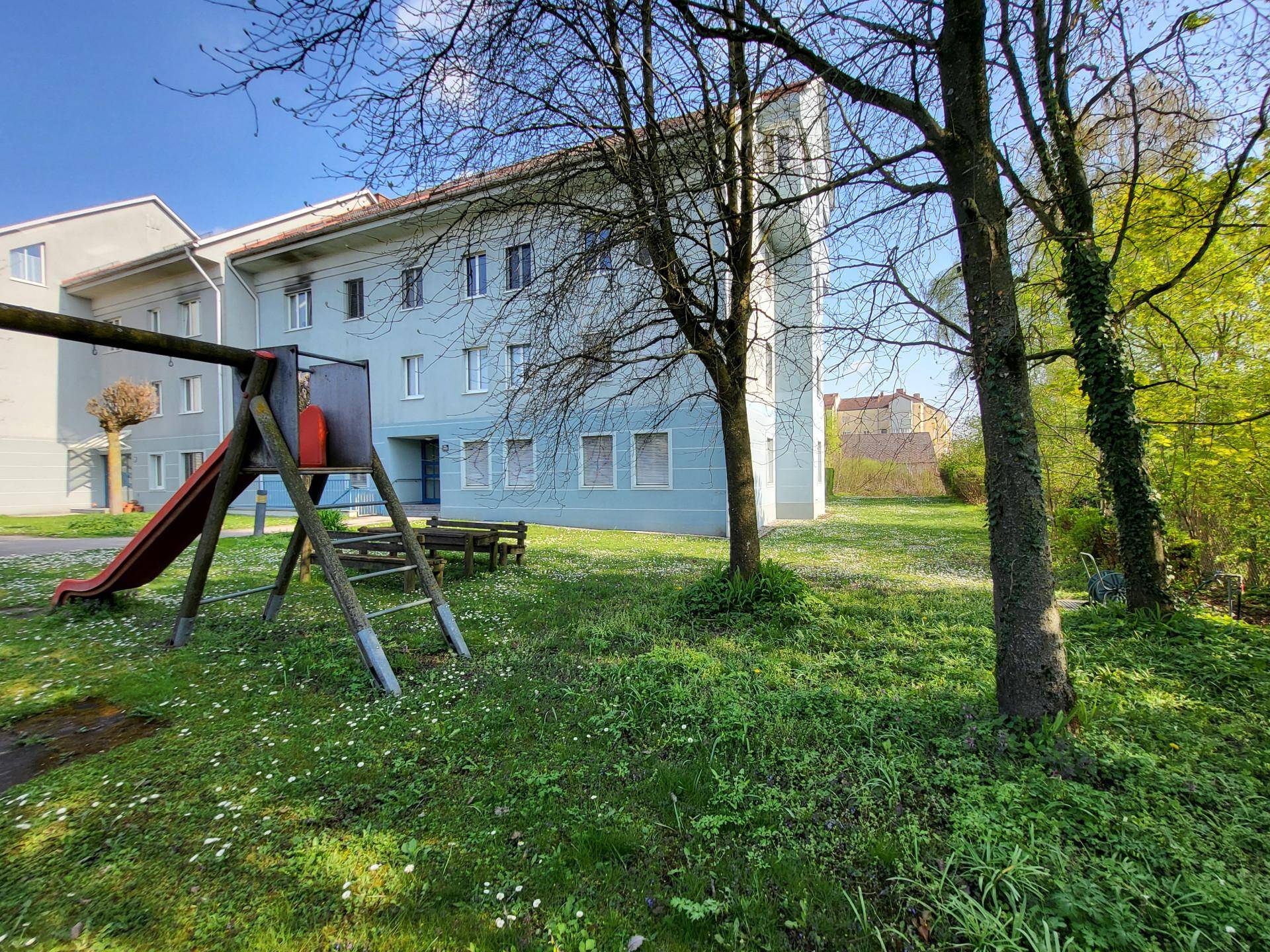 Außenansicht des Gebäudes mit angrenzendem Gemeinschaftsgarten und Kinderspielplatz.