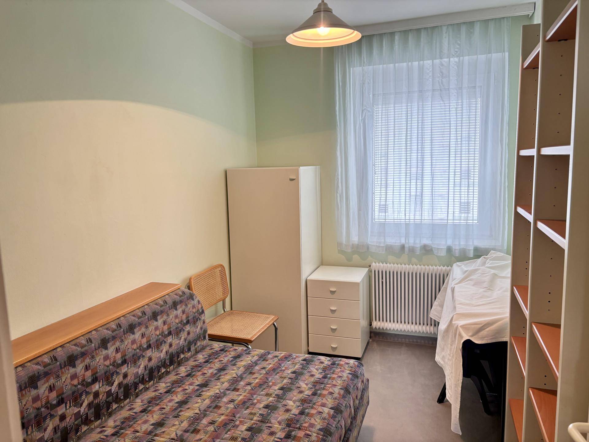 Helles Zimmer mit Schlafsofa, Heizkörper und Regalen, ideal als Gäste- oder Arbeitszimmer.
