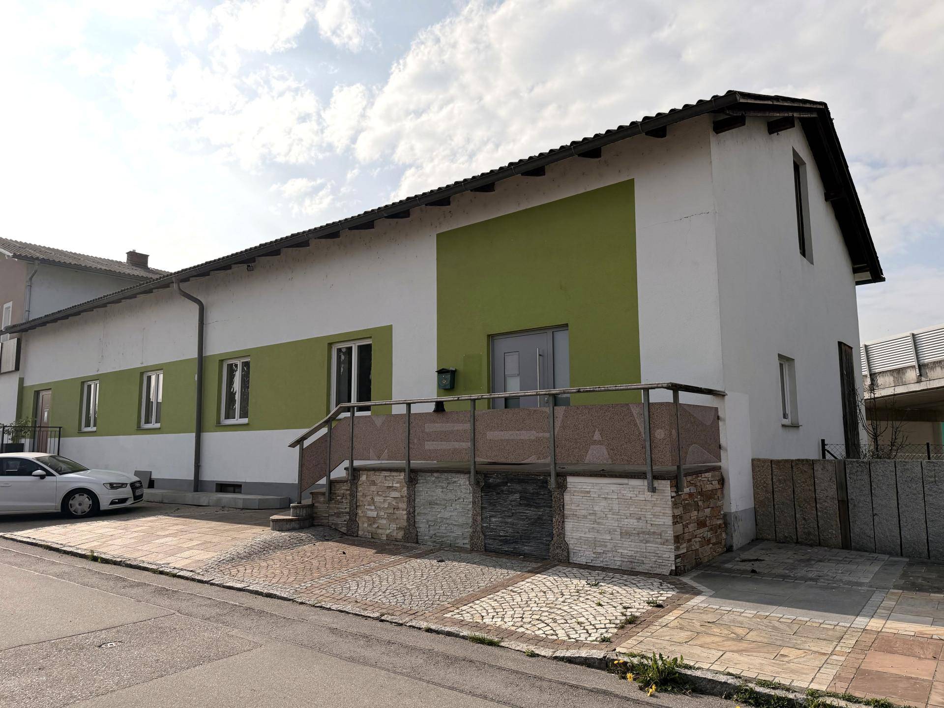 Außenansicht eines Gebäudes mit grün-weißer Fassade und einem kleinen Eingangsbereich.