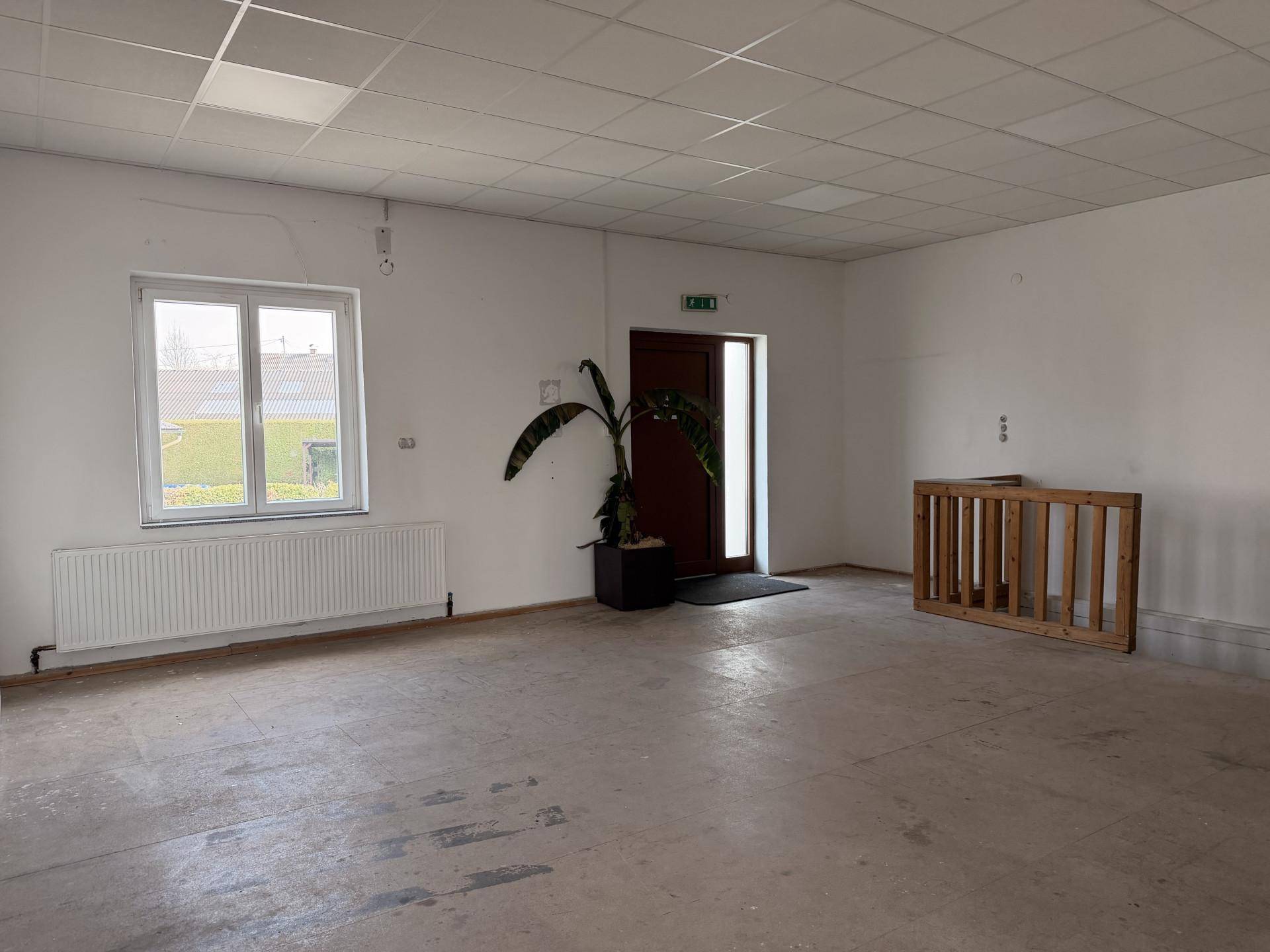 Geräumiger Gewerberaum mit abgehängter Decke, großem Fenster und einer Eingangstür.