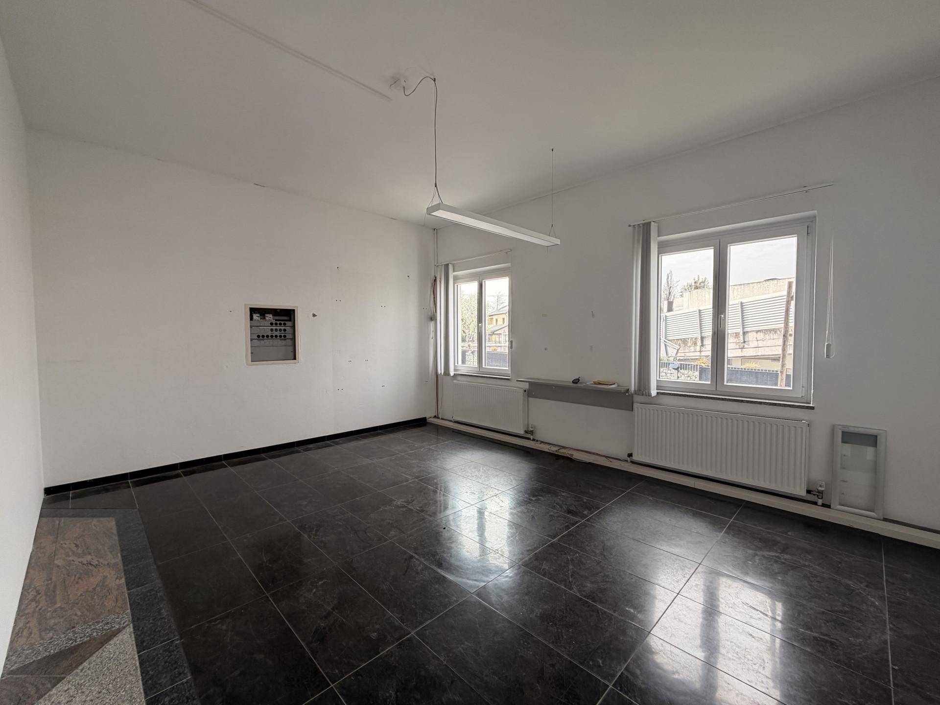 Heller Büroraum mit dunklem Fliesenboden, großen Fenstern und Heizkörpern.