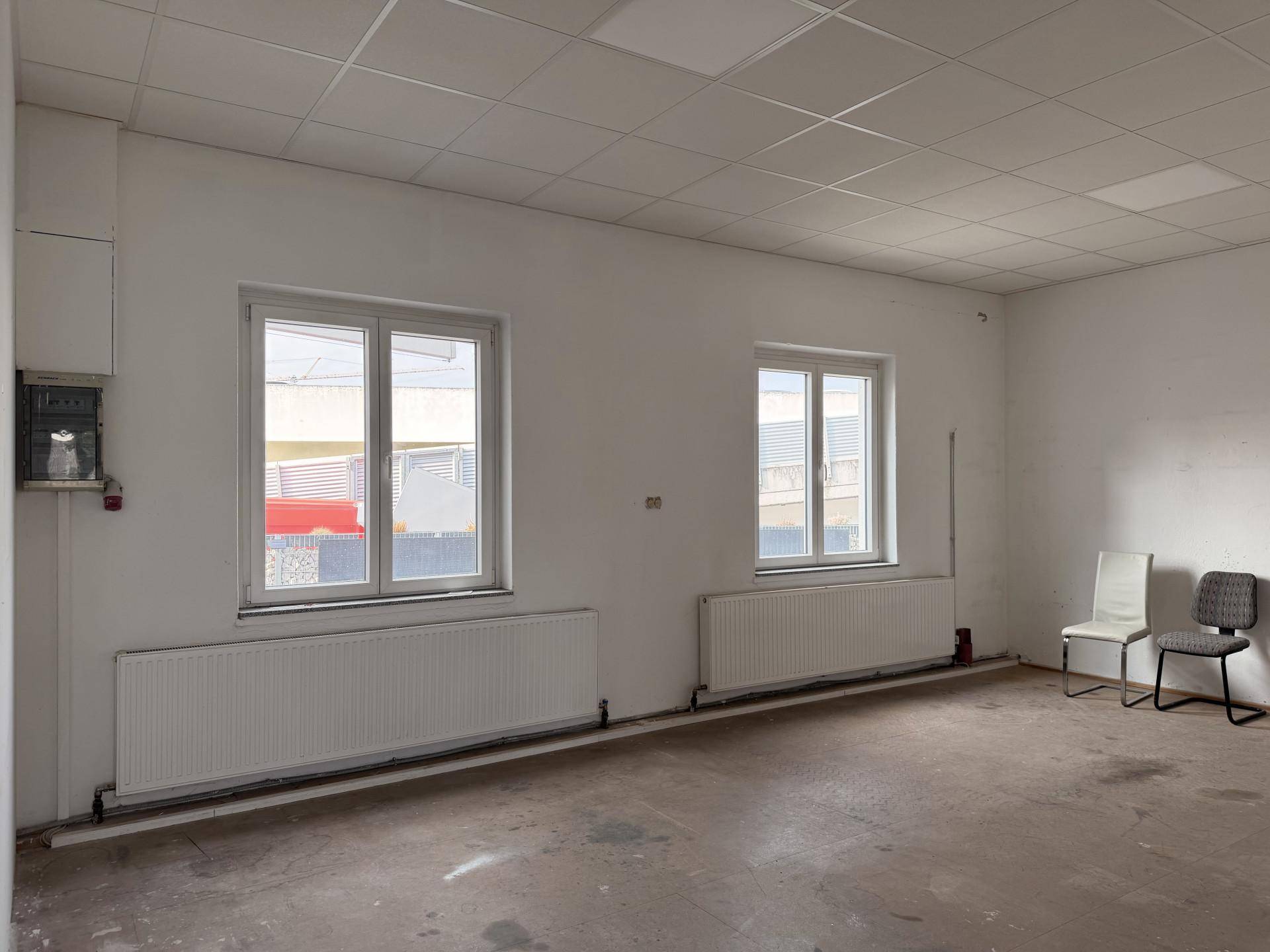 Heller Büroraum mit zwei großen Fenstern, Heizkörpern und einer abgehängten Decke.