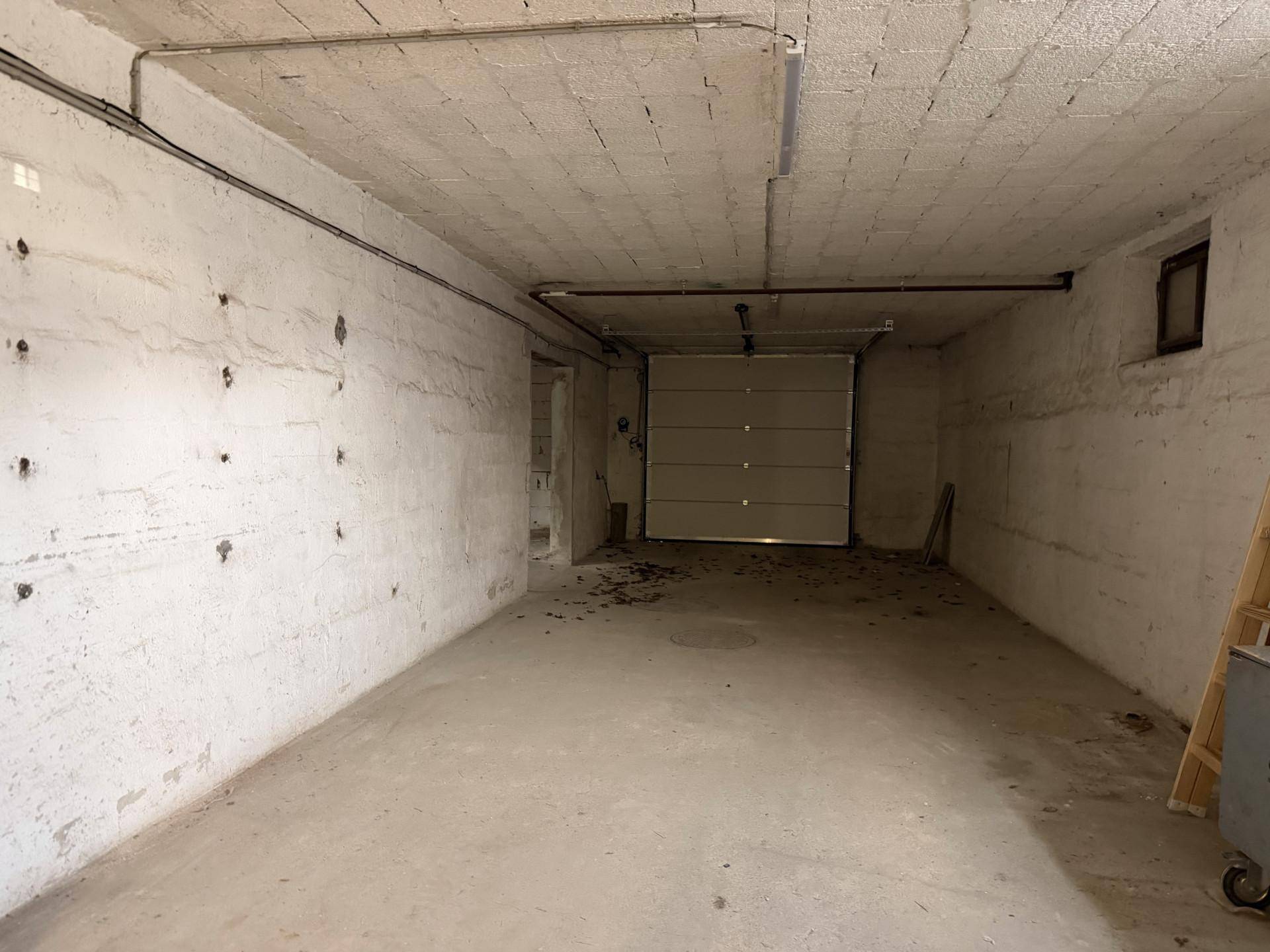 Geräumige Tiefgarage mit Rolltor, Betonboden und sichtbaren Leitungen an der Decke.