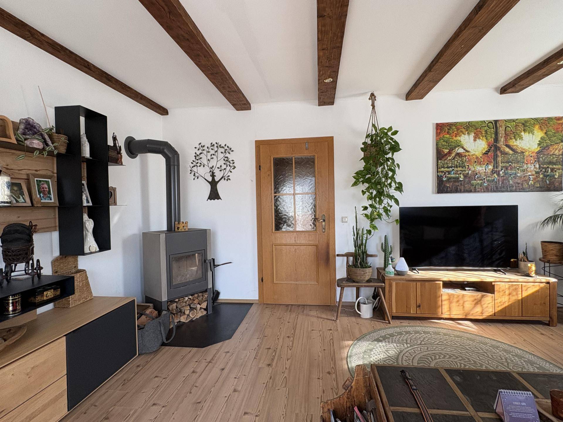 Helles Wohnzimmer mit Holzboden, Kaminofen und sichtbaren Deckenbalken.