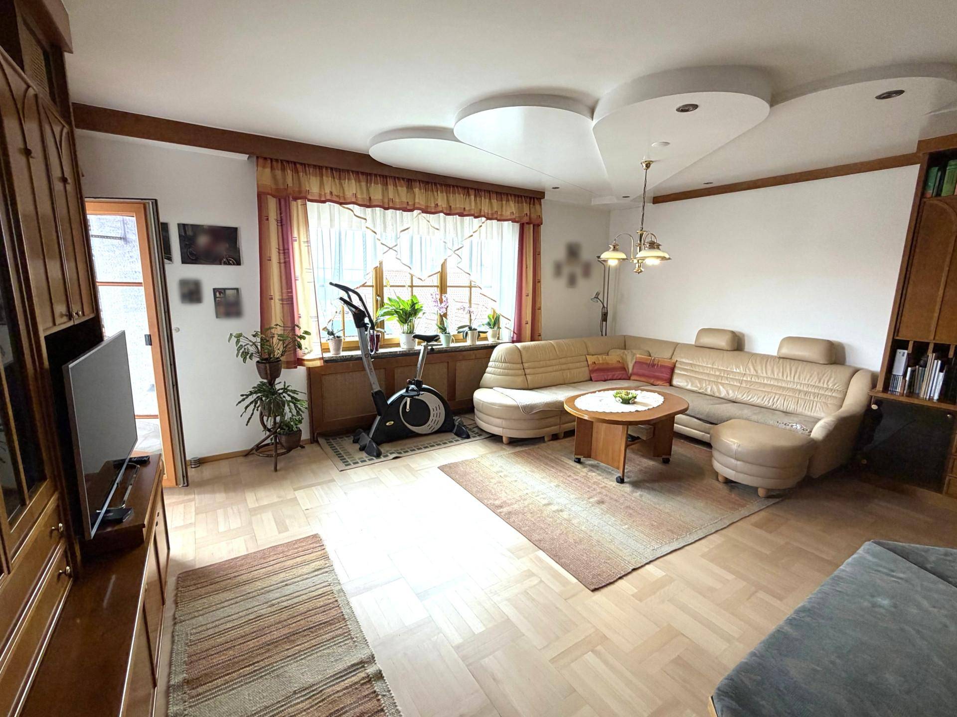 Helles Wohnzimmer mit beiger Ledercouch, Holzboden und dekorativen Deckenelementen.