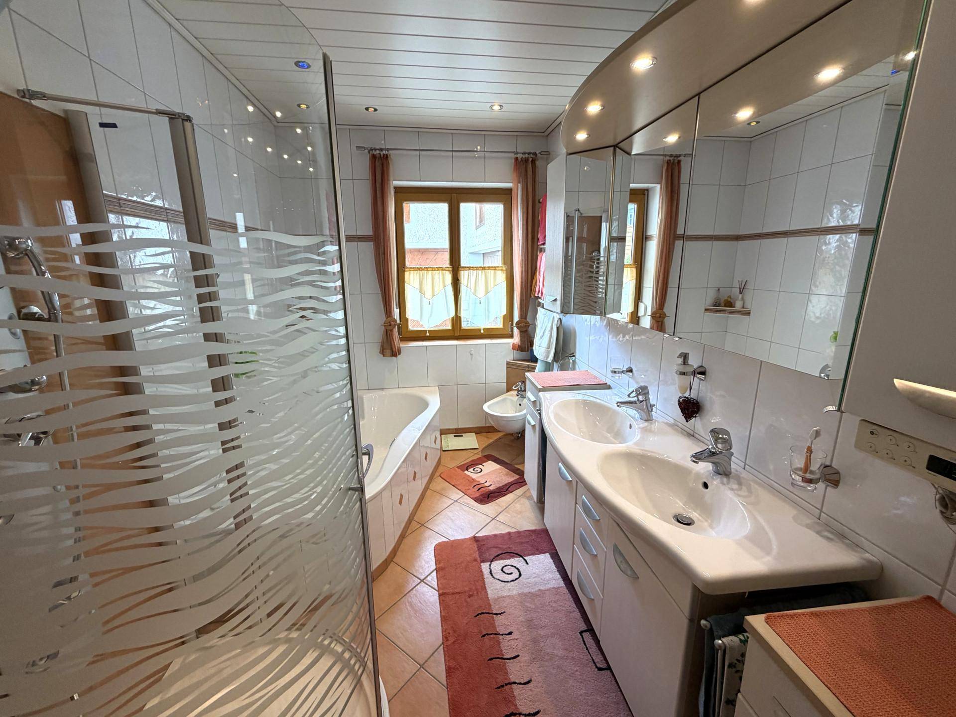 Badezimmer mit Doppelwaschbecken, Dusche, Badewanne und Fenster für Tageslicht.