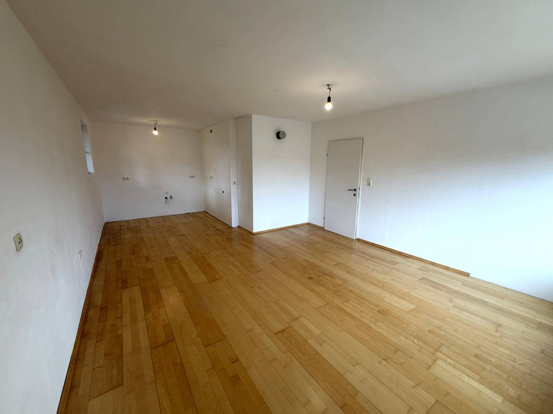 Geräumiger, leerer Raum mit hellem Holzboden und weißen Wänden, bereit zur Gestaltung.