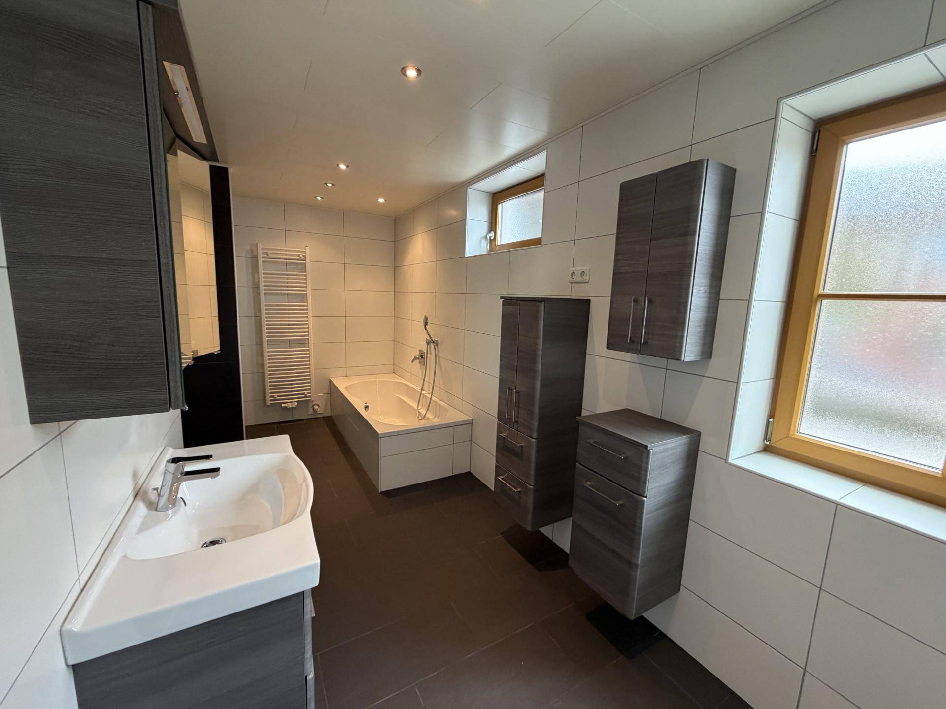 Modernes Badezimmer mit Badewanne, Einzelwaschbecken und grauen Schränken.
