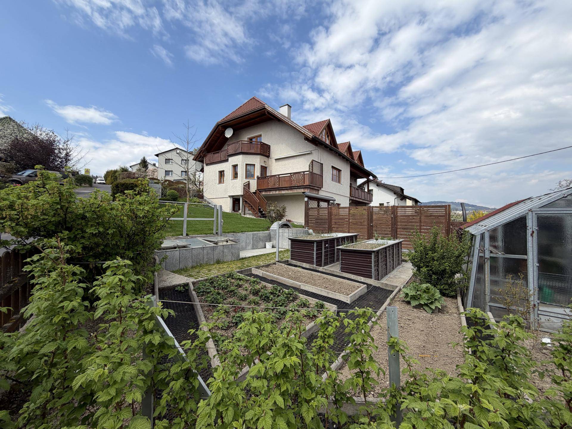 Gepflegter Gemüsegarten mit Hochbeeten und Gewächshaus neben dem Wohnhaus.