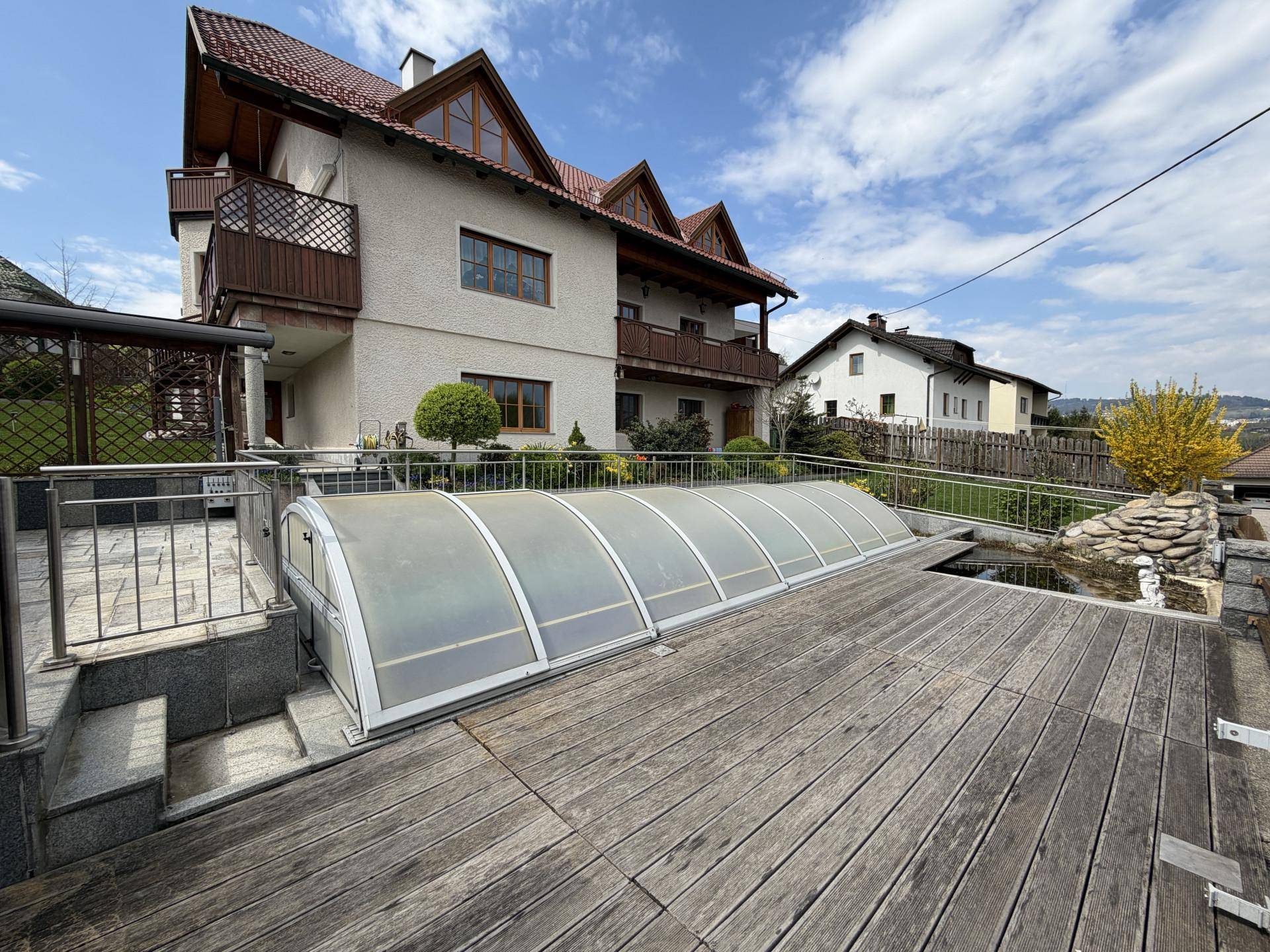 Große Holzterrasse mit überdachtem Pool und Blick auf die Umgebung.