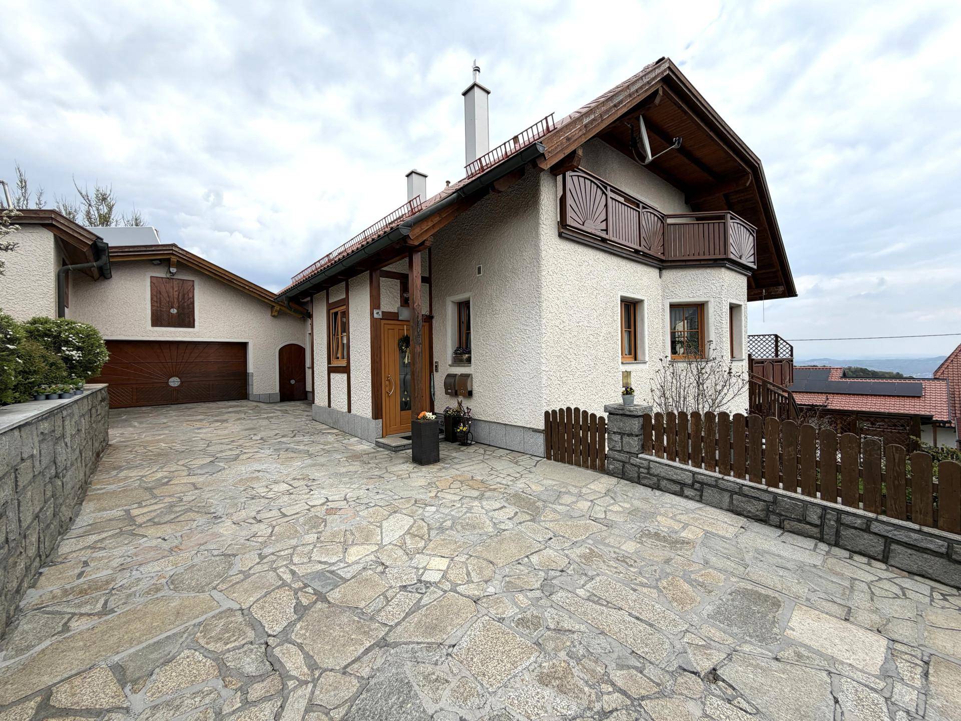 Vorderansicht des Hauses mit gepflasterter Auffahrt, Garage und traditionellen Holzelementen.