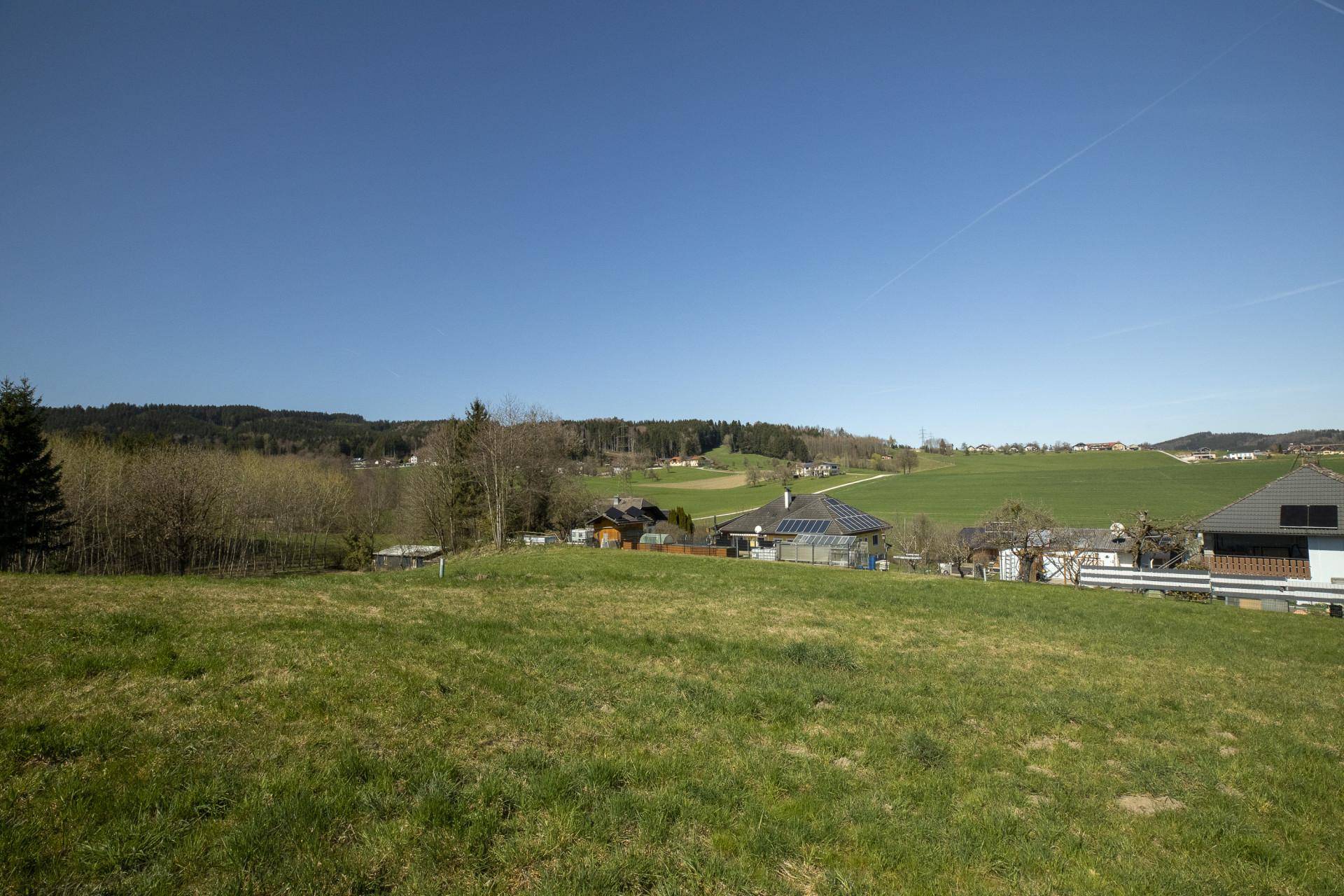 Baugrundstück mit Panoramablick auf die umliegende grüne Landschaft und verstreute Wohnhäuser.