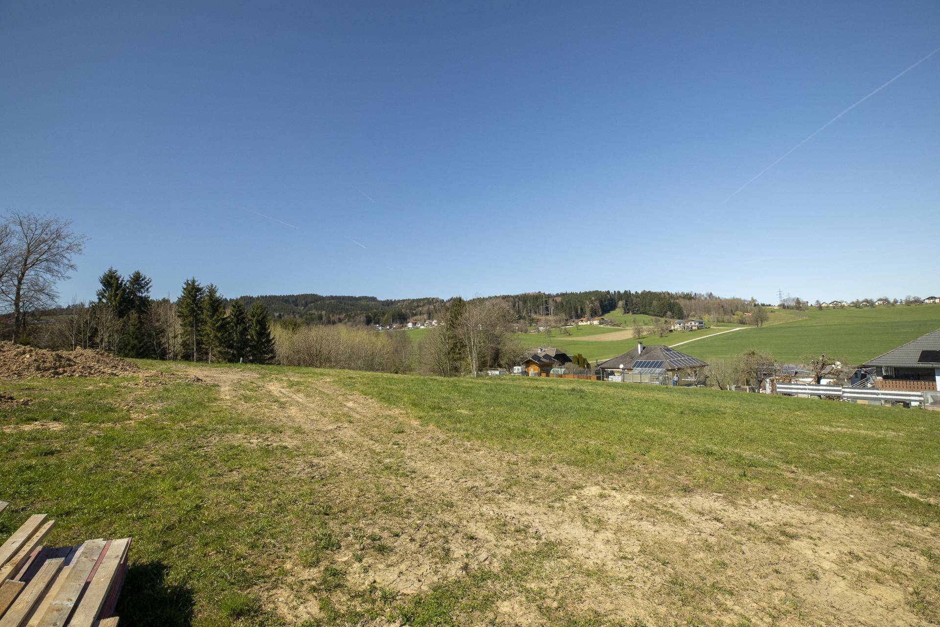 Unbebautes Grundstück mit Blick auf die weite grüne Landschaft und einige Bäume am Horizont.