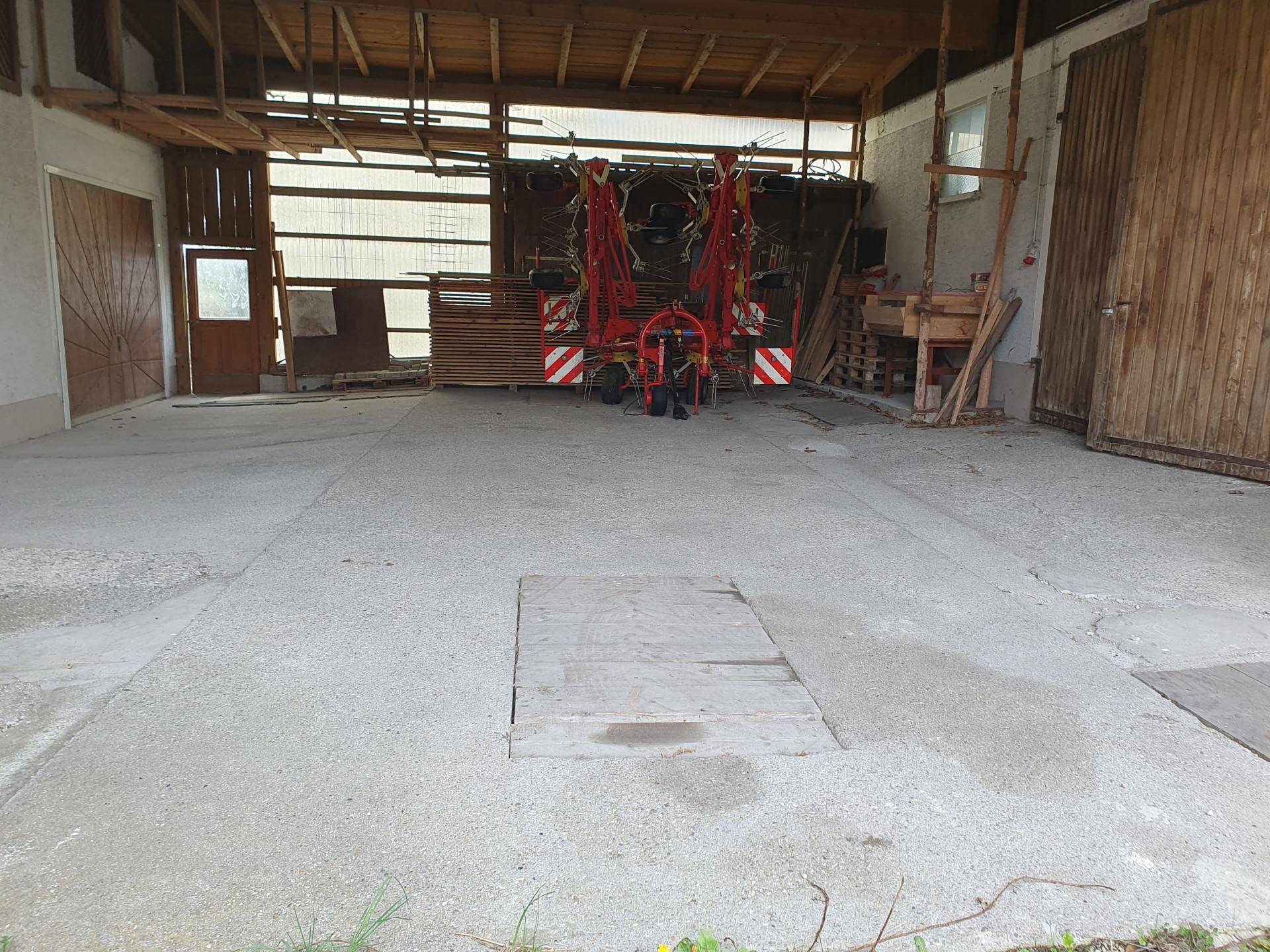Geräumiger Scheunenbereich mit Betonboden, Holzbalken und landwirtschaftlichen Geräten.
