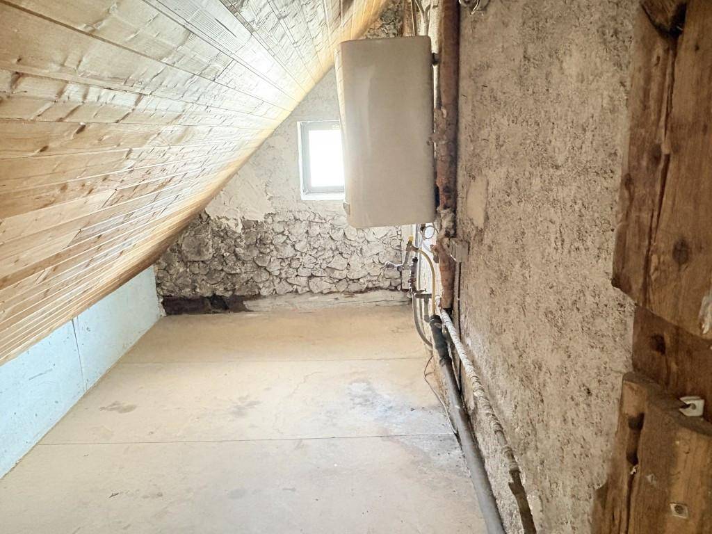 Unausgebauter Dachboden mit Holzbalken, Steinwand und kleinem Fenster, ideal für Ausbau.
