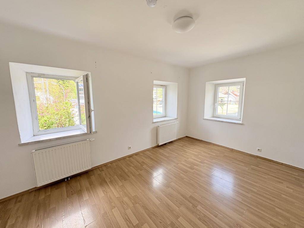 Lichtdurchfluteter Raum mit Holzboden, weißen Wänden und geöffnetem Fenster.
