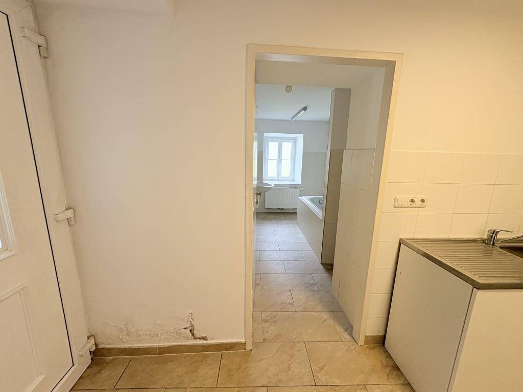 Flur oder Hauswirtschaftsraum mit Fliesenboden und Blick in ein angrenzendes Badezimmer.