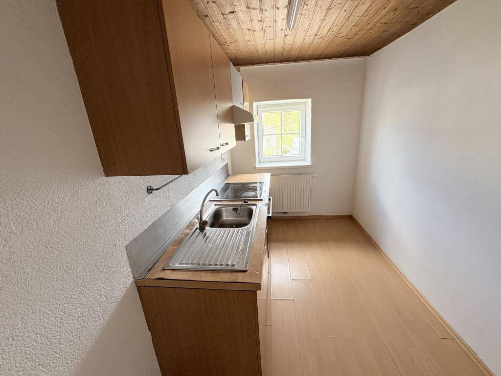 Kleine Küche mit Holzschränken, Spüle, Kochfeld und einer Holzdecke.