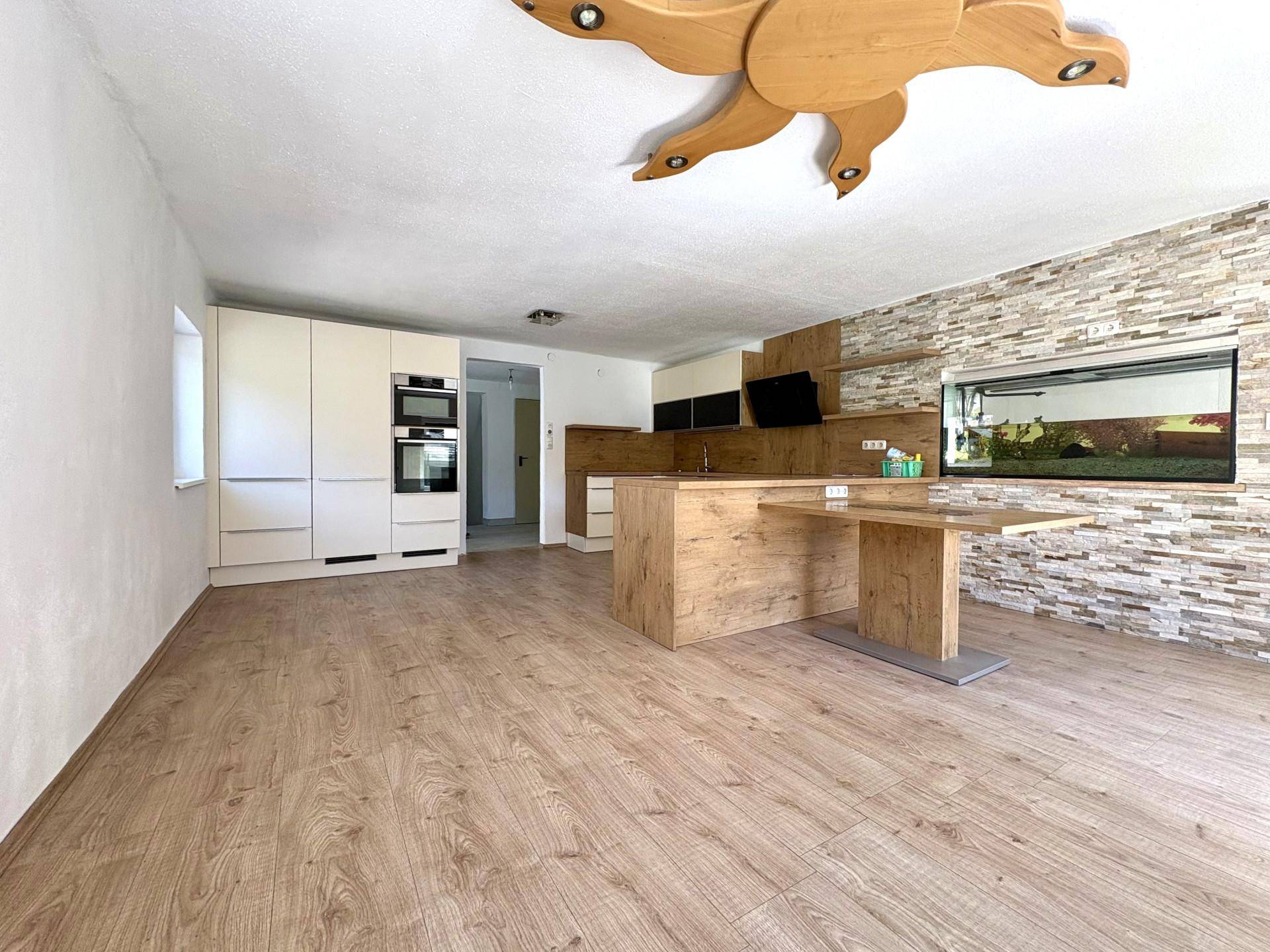 Geräumiger Wohn- und Essbereich mit integrierter Küche, Holzboden und dekorativer Steinwand.