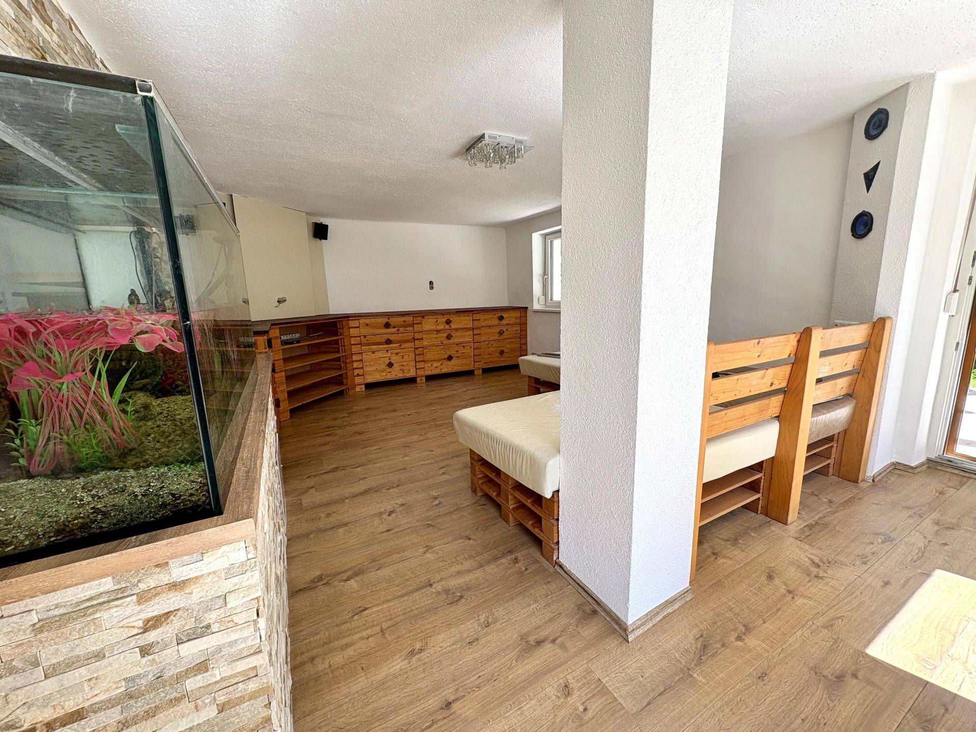 Gemütlicher Wohnbereich mit Holzbänken, Aquarium und Blick auf den Garten.