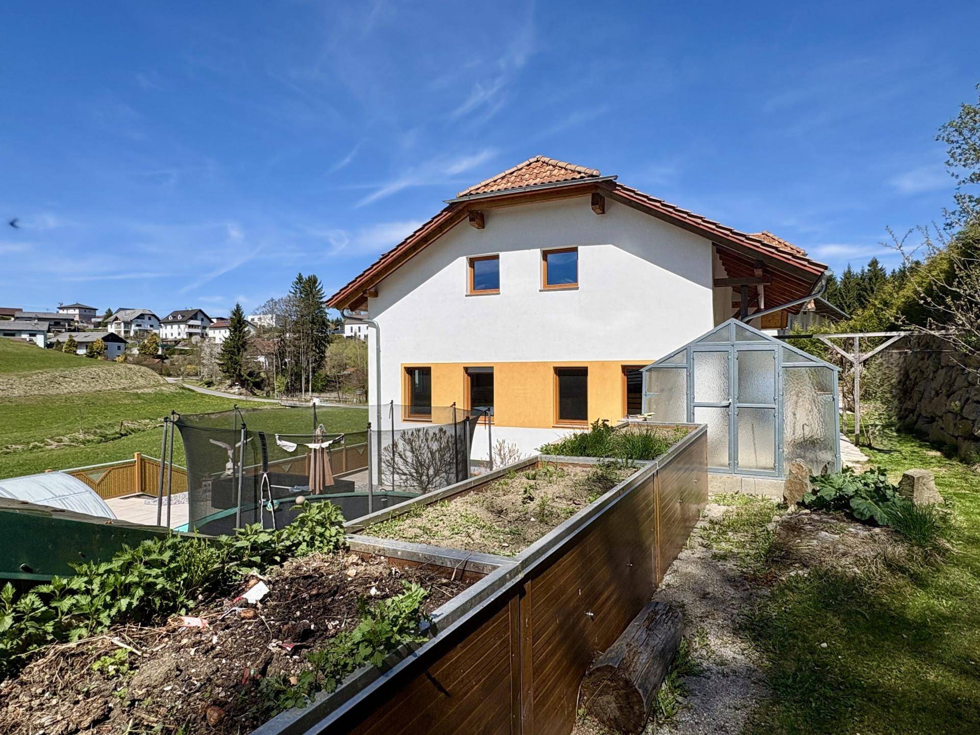 Gepflegter Gartenbereich mit Hochbeeten, Gewächshaus und Blick auf das Wohnhaus.