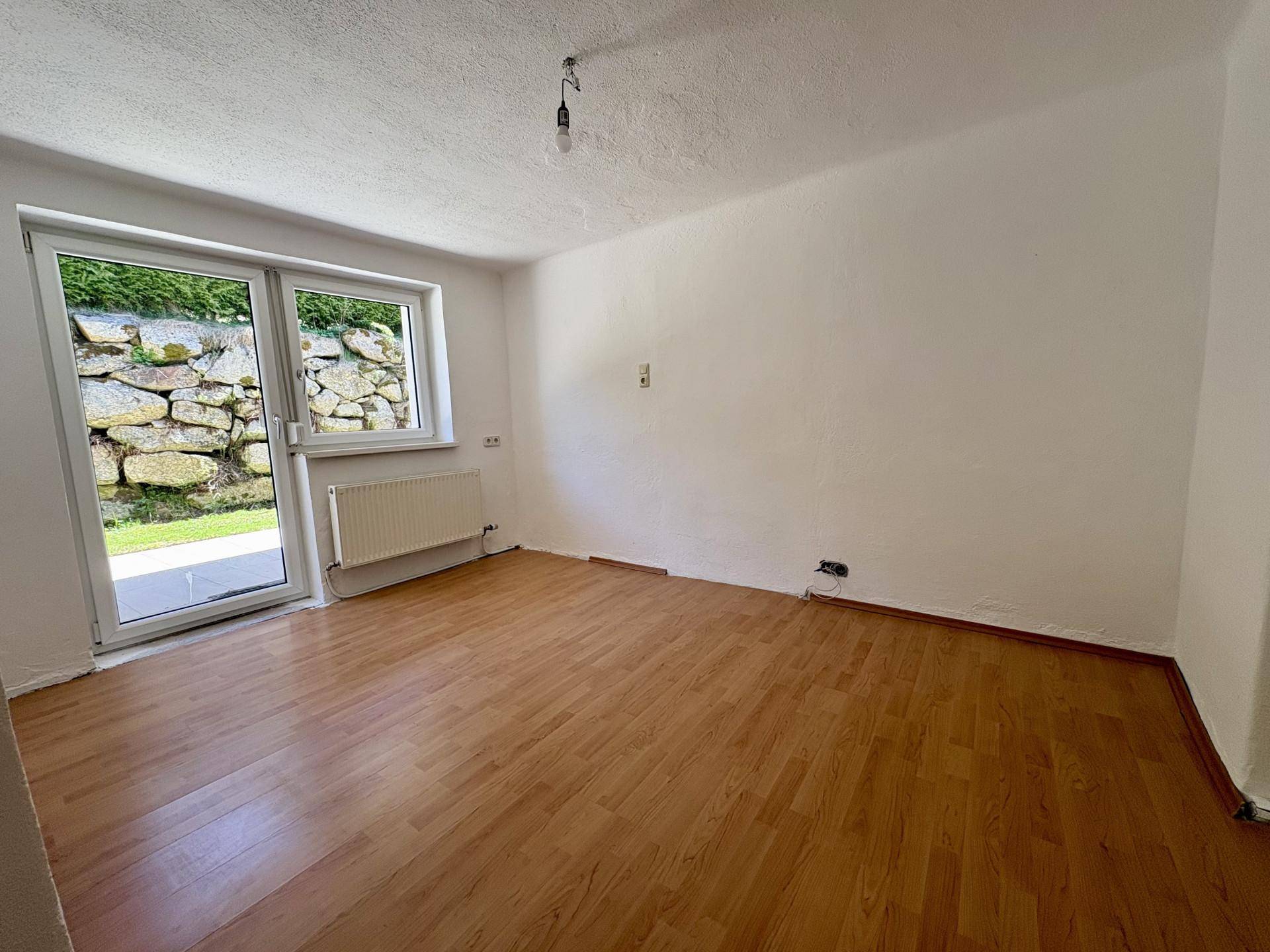Helles Zimmer mit Holzboden und direktem Zugang zum Außenbereich mit Steinmauer.