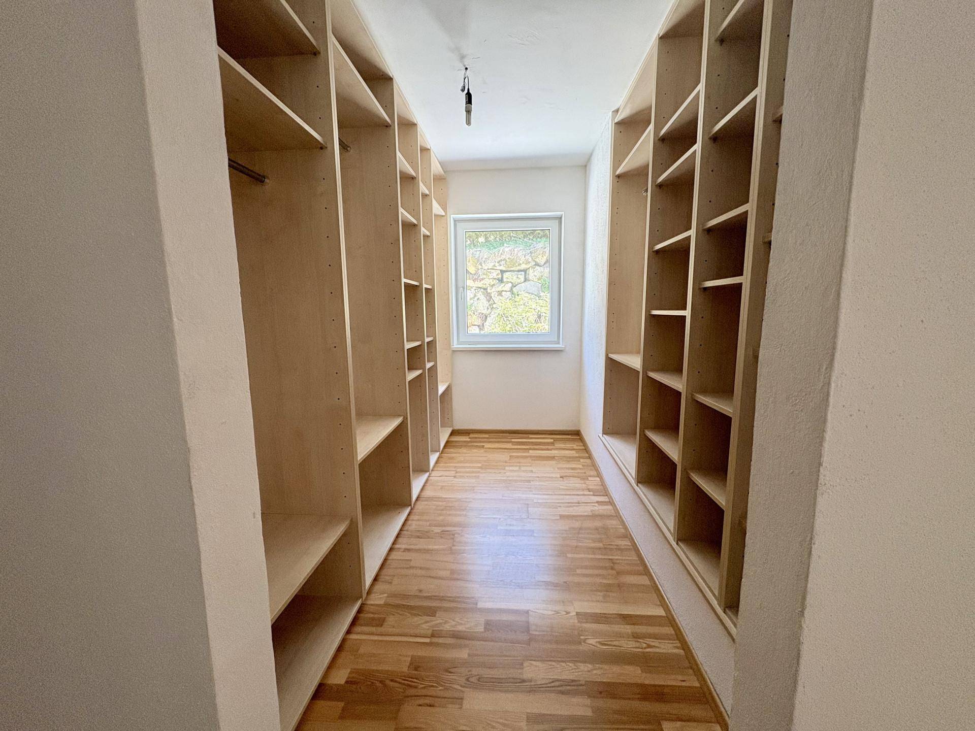 Geräumiger begehbarer Kleiderschrank mit vielen Regalen und Fenster für Tageslicht.
