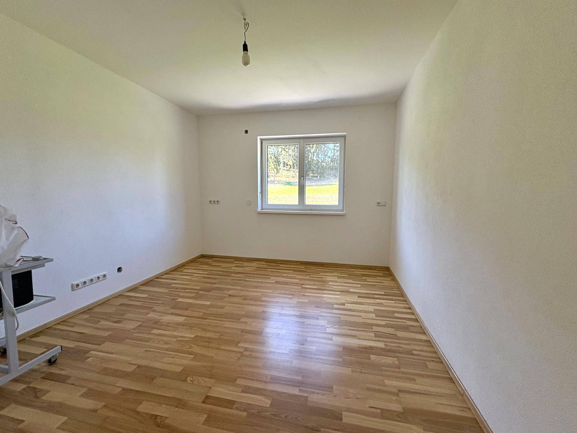 Helles Schlafzimmer mit Holzboden und Fenster mit Blick ins Grüne.
