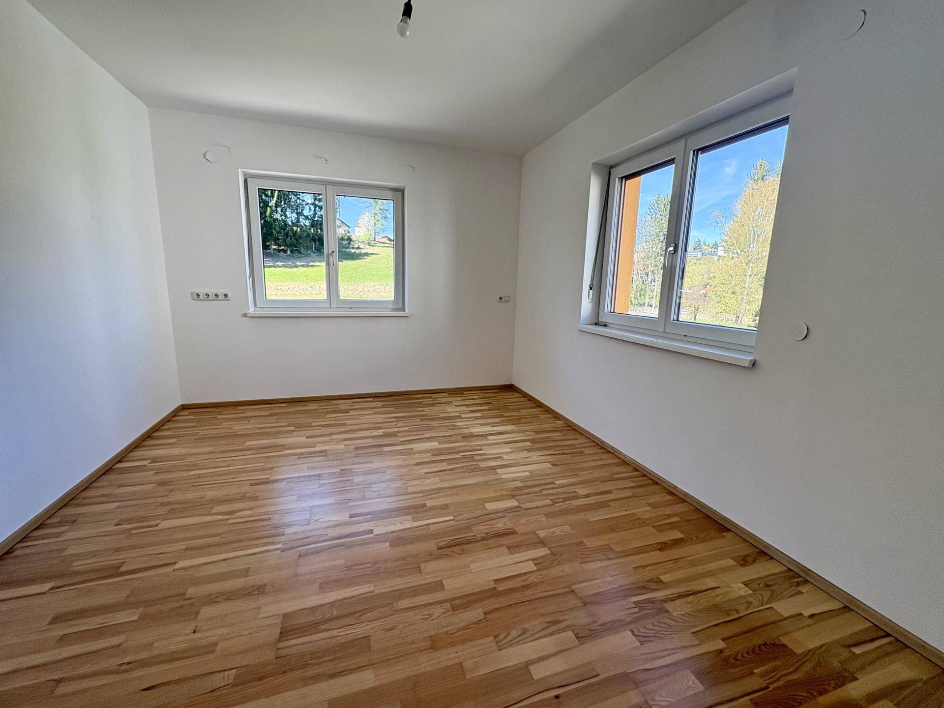 Lichtdurchflutetes Zimmer mit Holzboden und zwei Fenstern für viel Tageslicht.